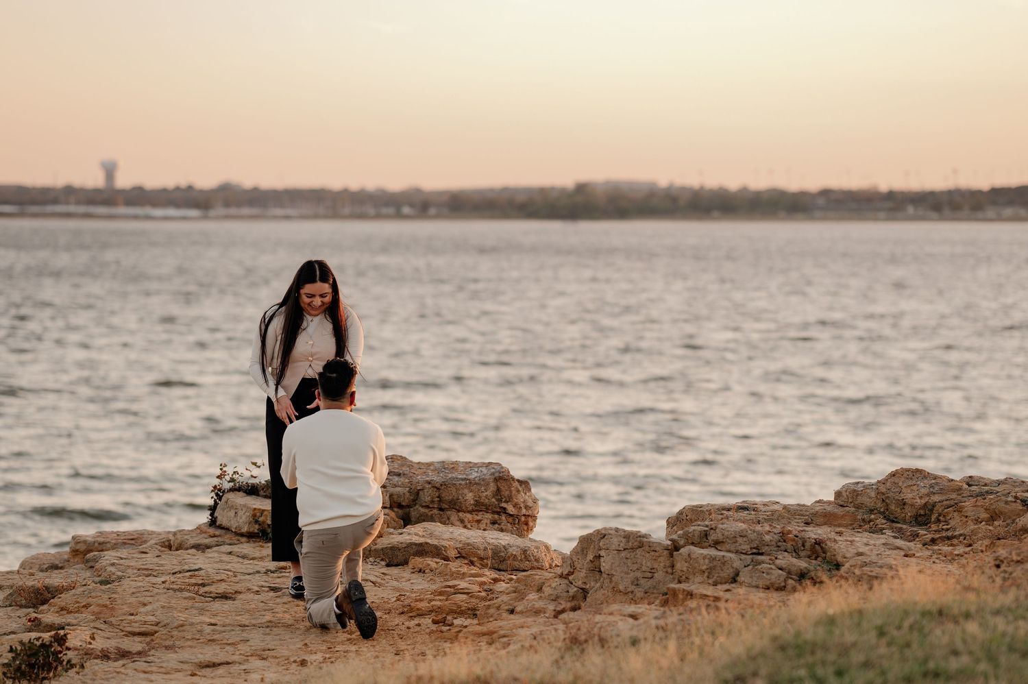 Romantic surprise proposal for a couple overlooking large lake on a rocky cliff in Grapevine Texas at golden hour