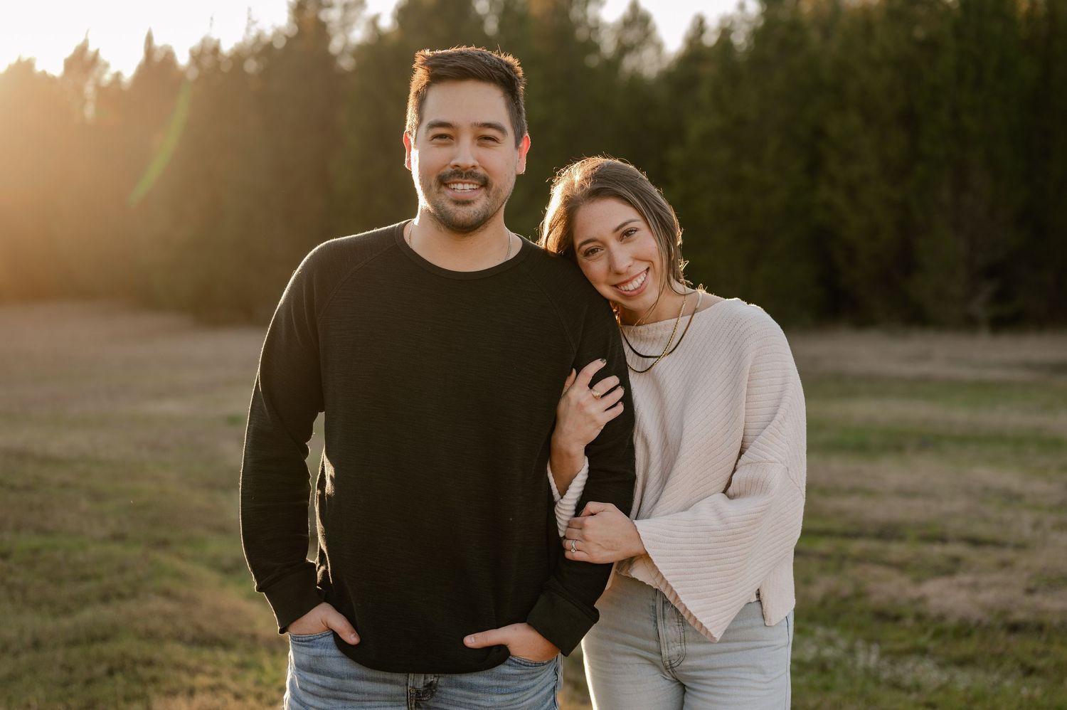 Joyful couple posing while wife hugs husband's arm at a couple's photo session in a large tree lined field in Sunnyvale, Texas