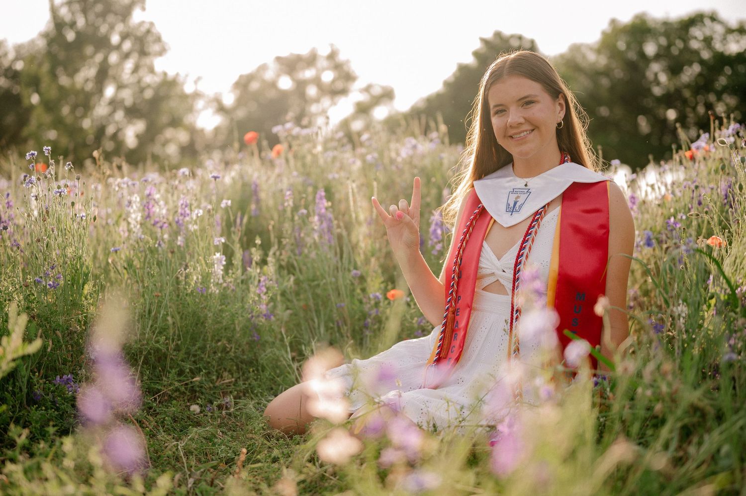 Senior girl sitting in a wildflower patch in her graduation stoles for a Spring summer photo session in Richardson, Texas