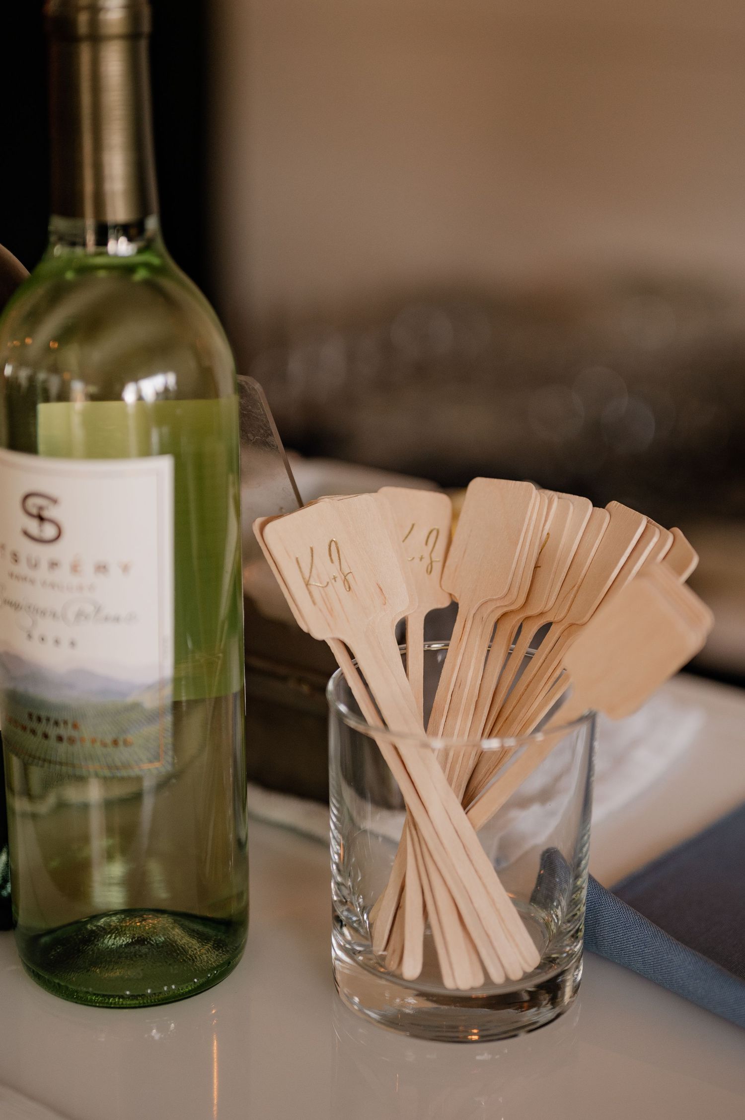 Wedding detail photo of wine bottle and glass filled with wooden drink stirrers on counter