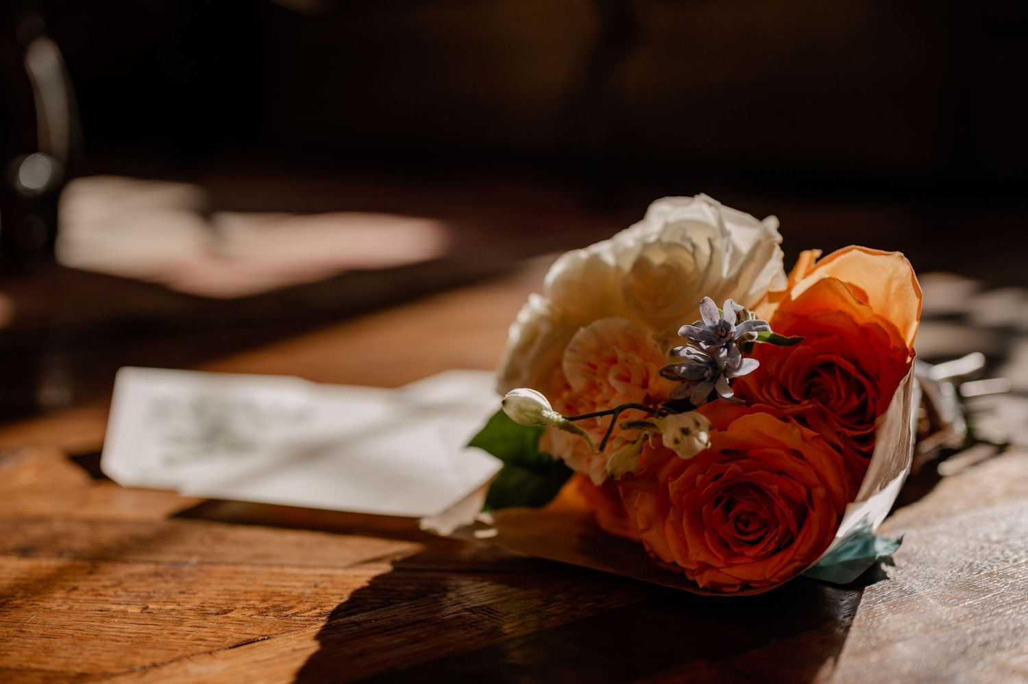 A colorful wedding bouquet with orange roses and blue flowers resting on a wooden table.