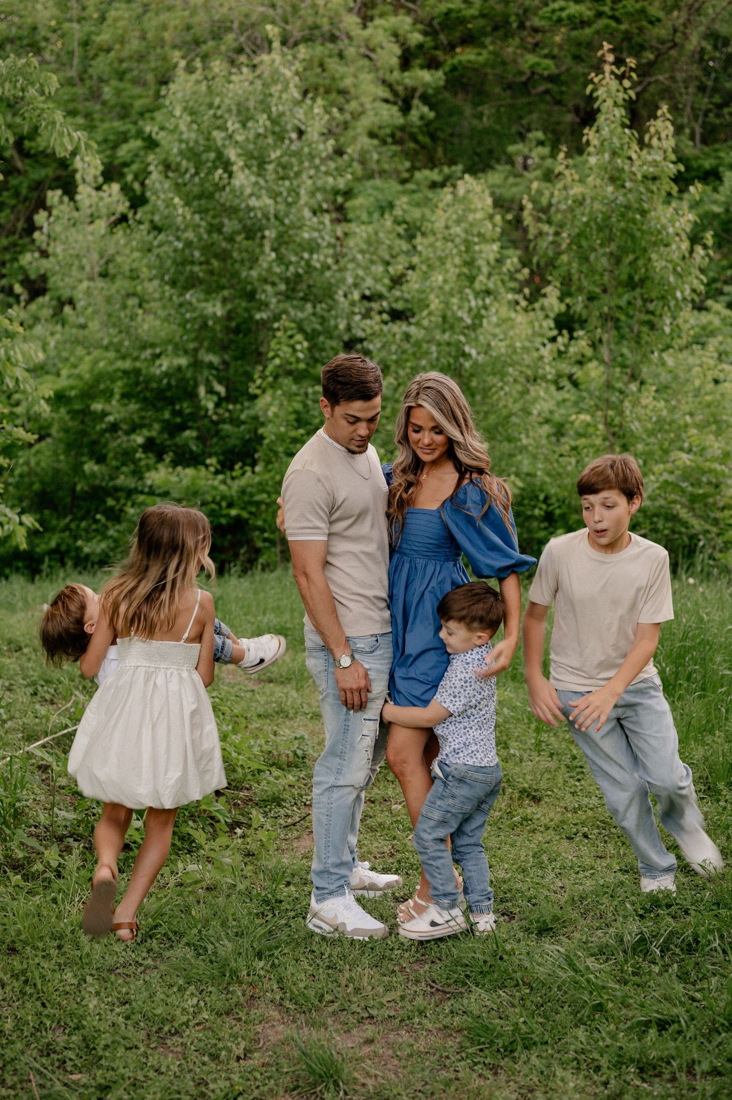 Wide shot of a family of 6 with kids running playfully in a circle around mom and dad in a green Spring field in Garland, Texas