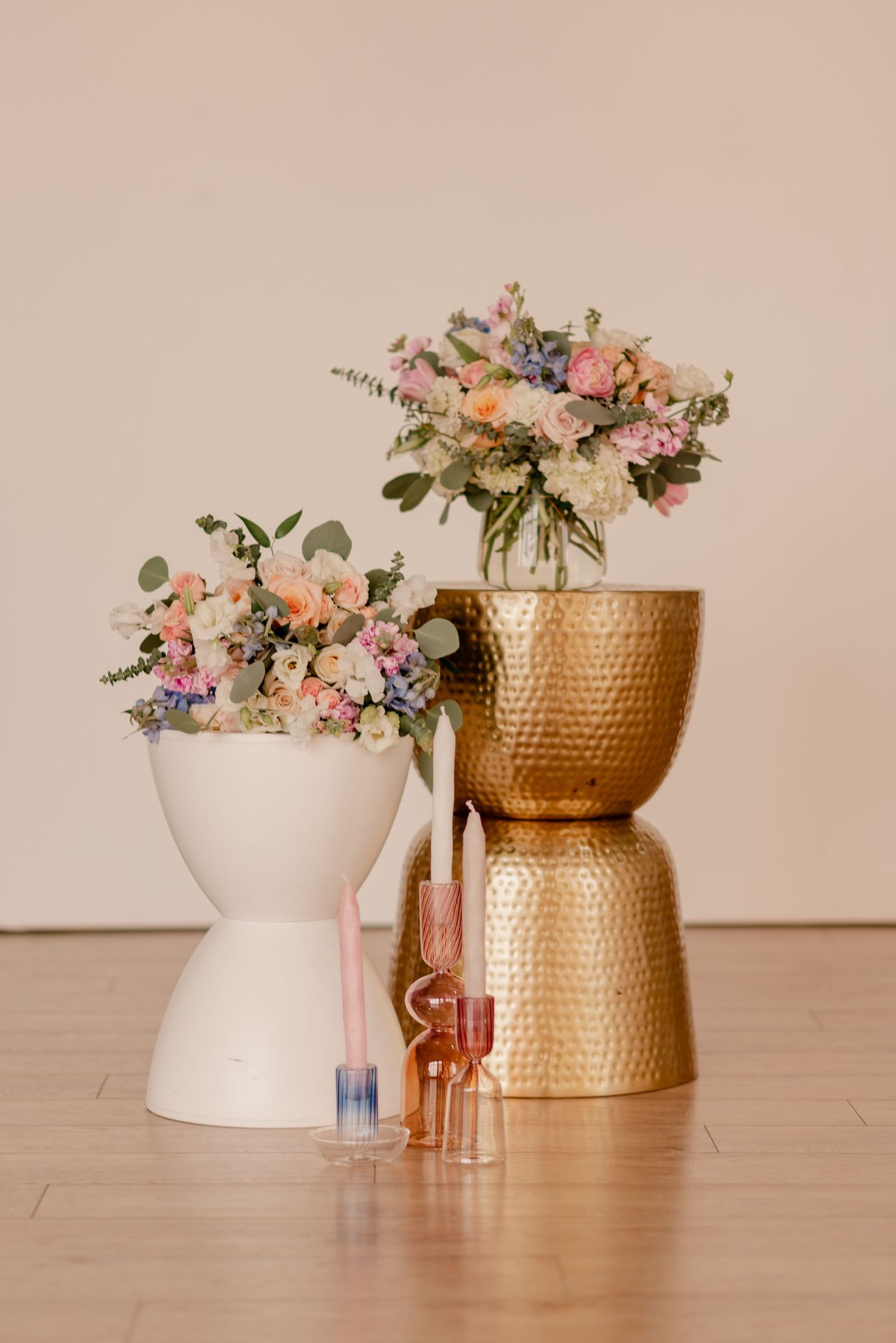 Pastel wedding floral arrangements in gold and white modern vases against neutral background.