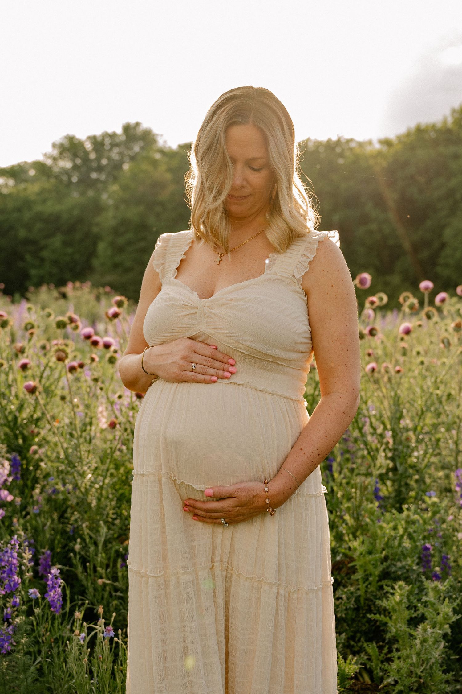 Intimate candid moment of woman holding pregnant belly in a wide wildflower field for a summer maternity session in Richardson, Texas