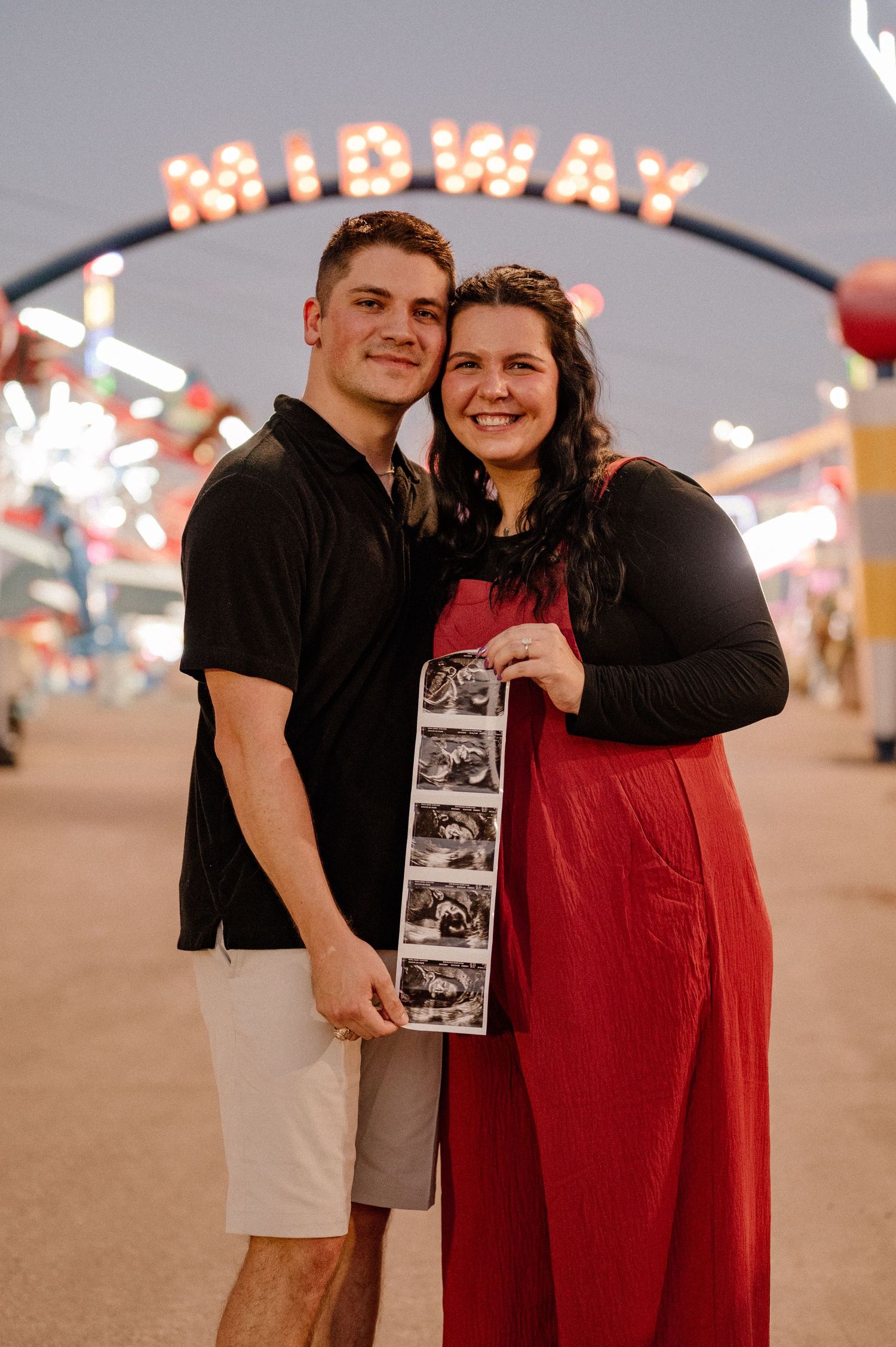 Couple posing with a sonogram at the State Fair of Texas Midway for their fall pregnancy announcement and maternity photos