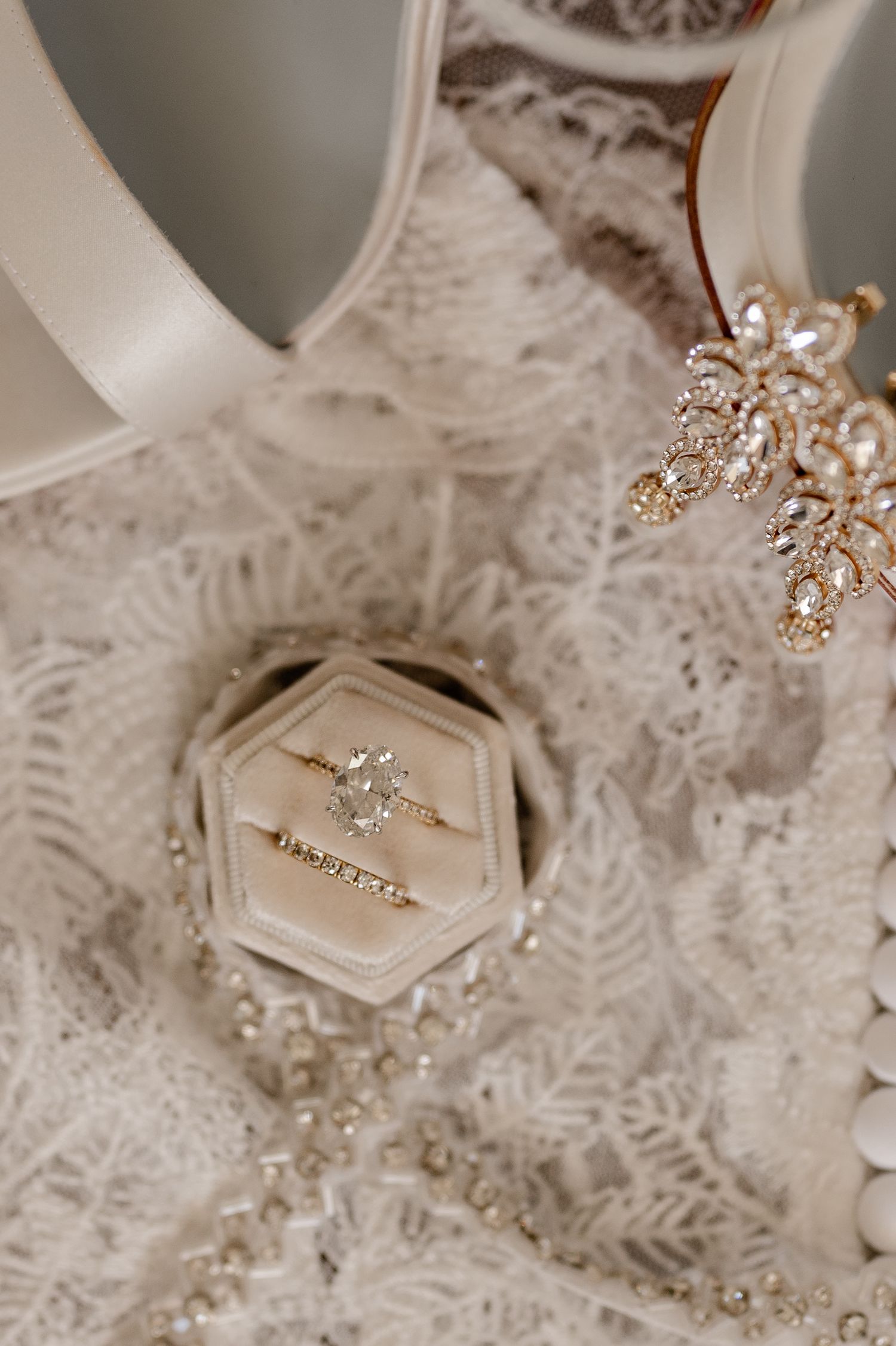 Delicate lace backdrop with sparkling crystal jewelry and wedding ring in a box in soft neutral tones.