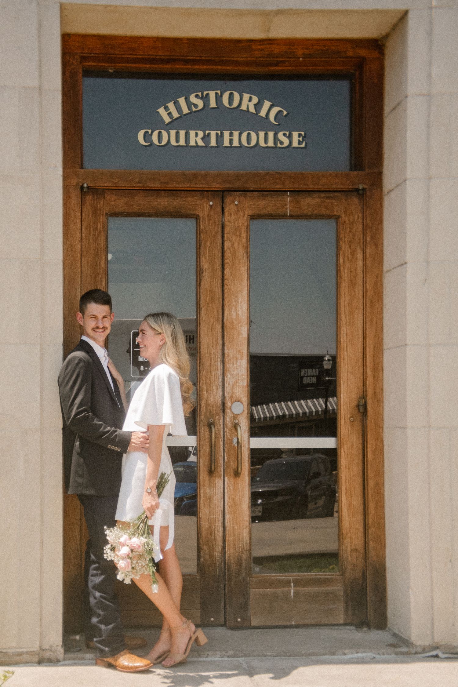 Film photo of couple posing outside in front of the downtown Rockwall courthouse during a summer elopement wedding photo session
