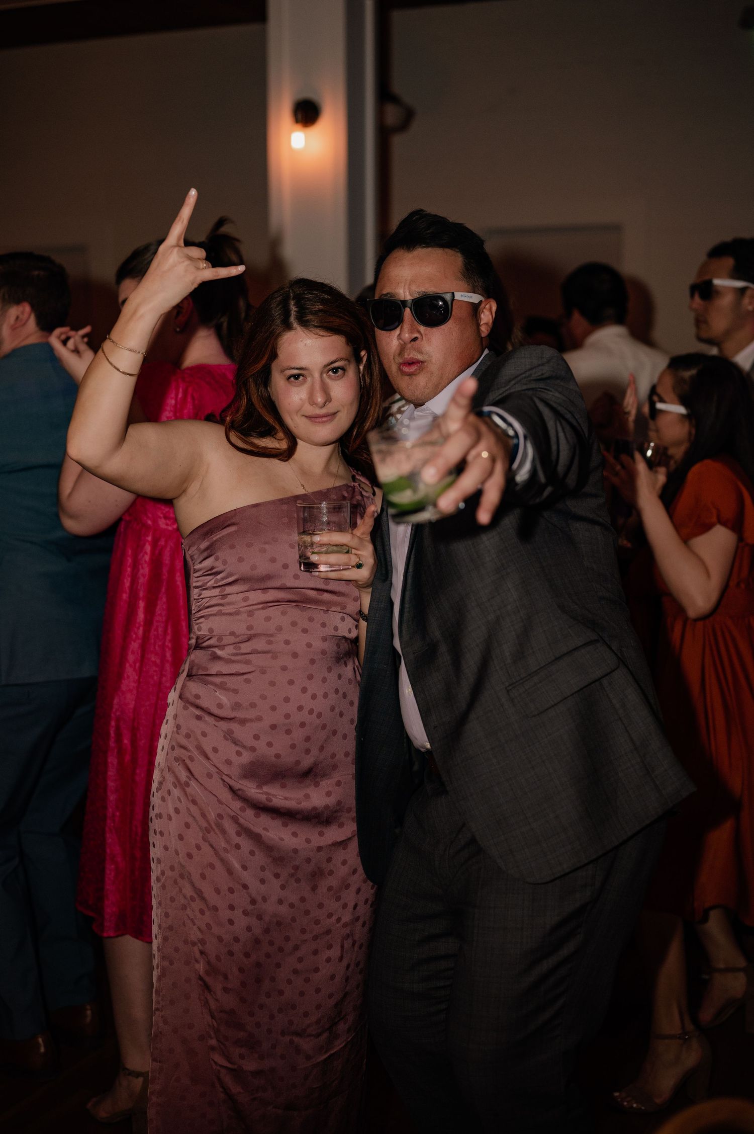 Party guests in formal attire dancing and posing with drinks at wedding reception