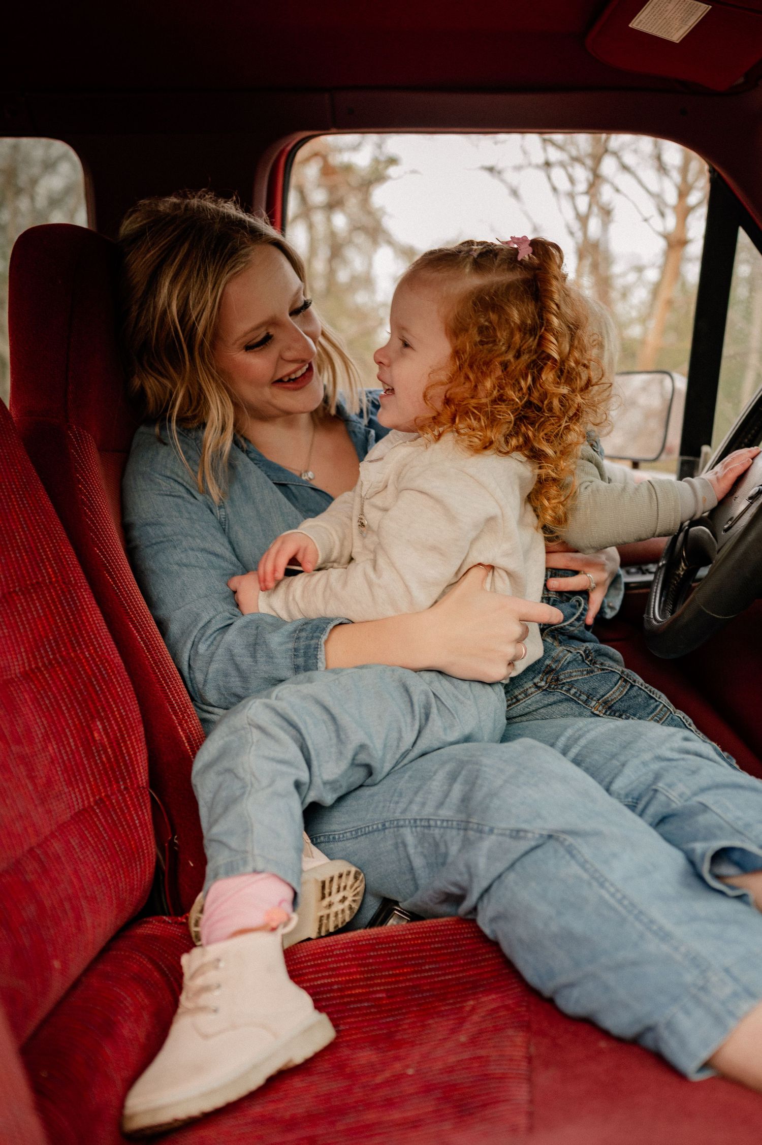 Mom and daughter candidly cozied up in the cab of a red vintage truck for a winter family photo session