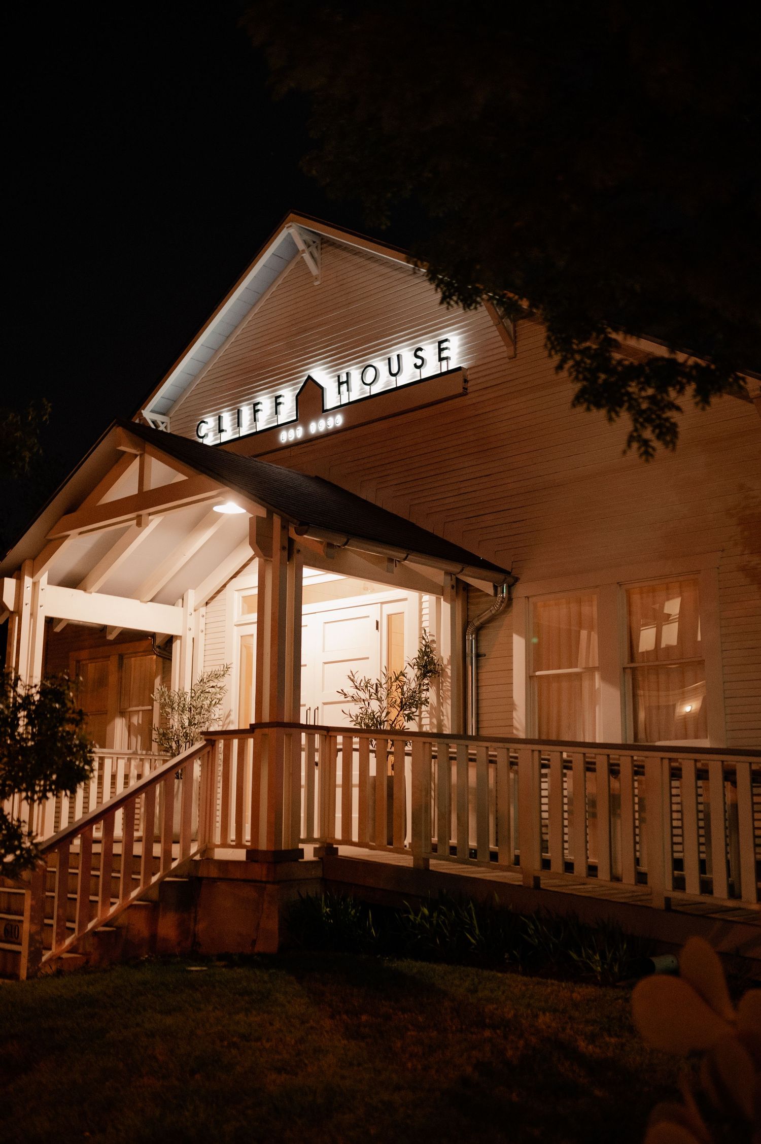 A white country house with wrap-around porch illuminated at night creates a warm, inviting atmosphere.