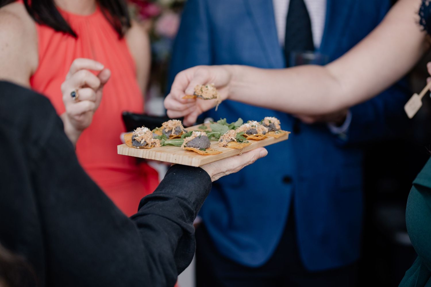 Wedding party members stand at a formal reception while a server carries appetizers on a tray.