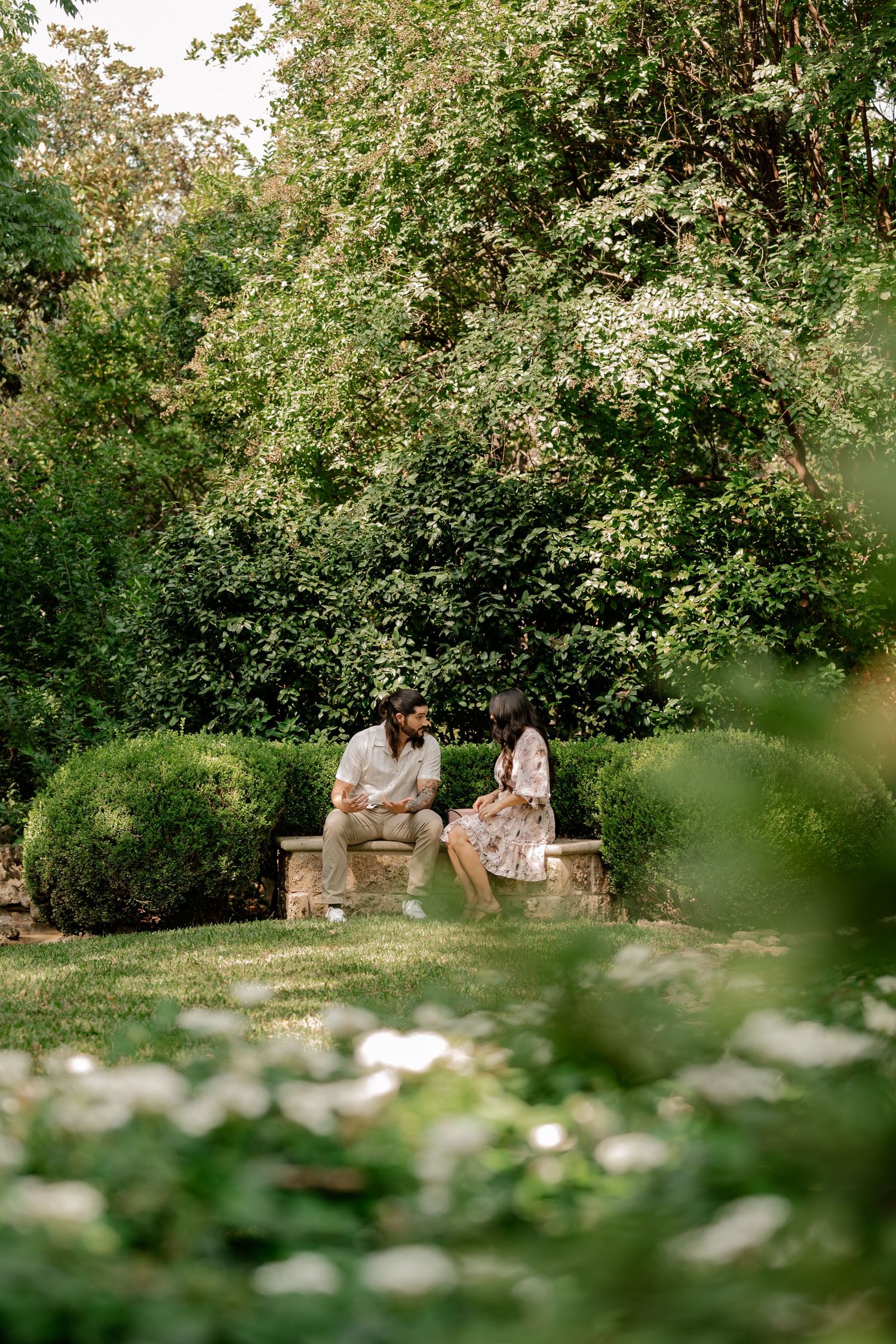 Candid image of couple surrounded by green trees and flowers during a proposal couple's session at the Dallas Arboretum in East Dallas