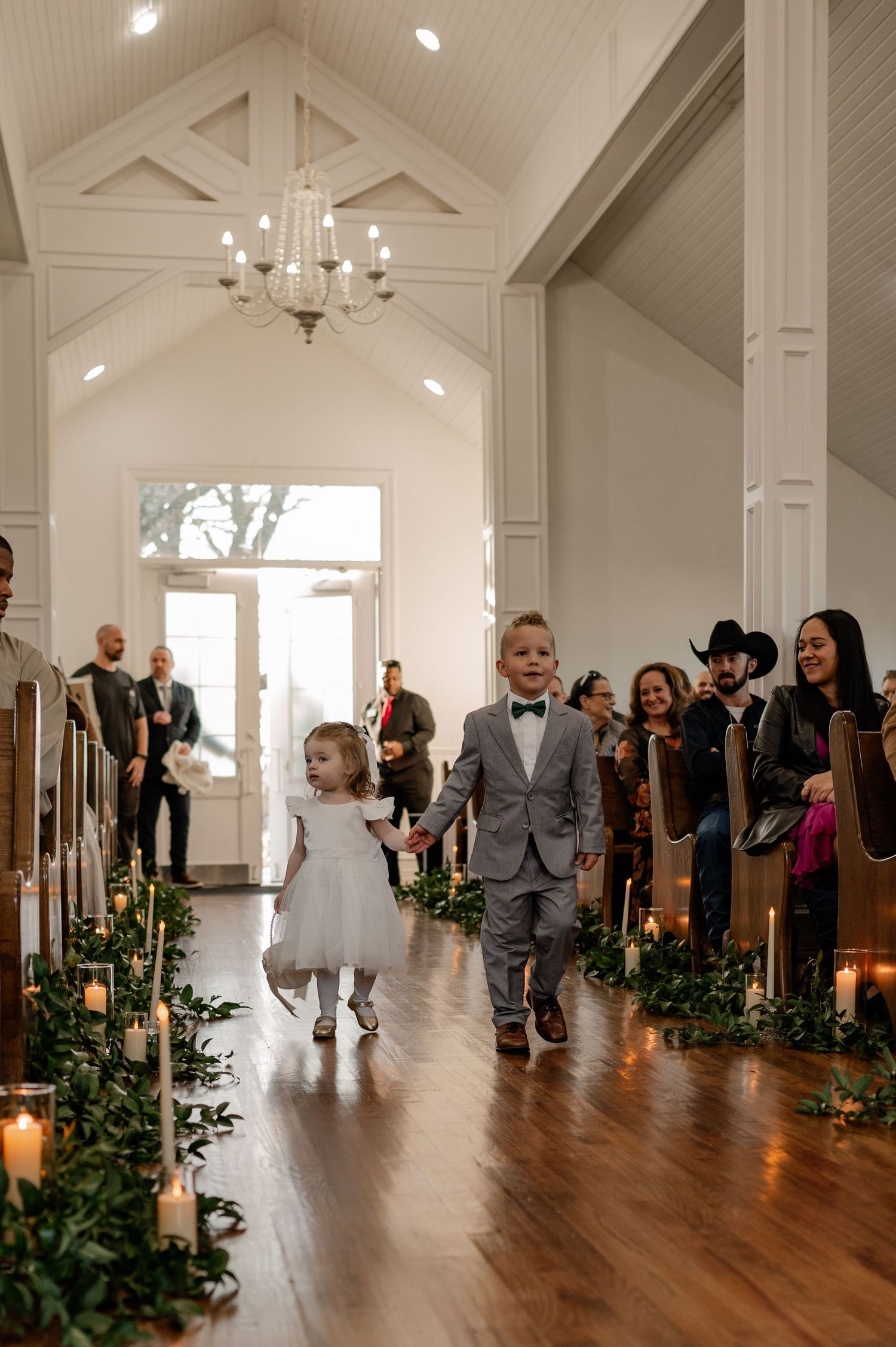 Candid photo of a small ring bearer and flower girl coming down the aisle of an indoor wedding chapel in Denton, Texas