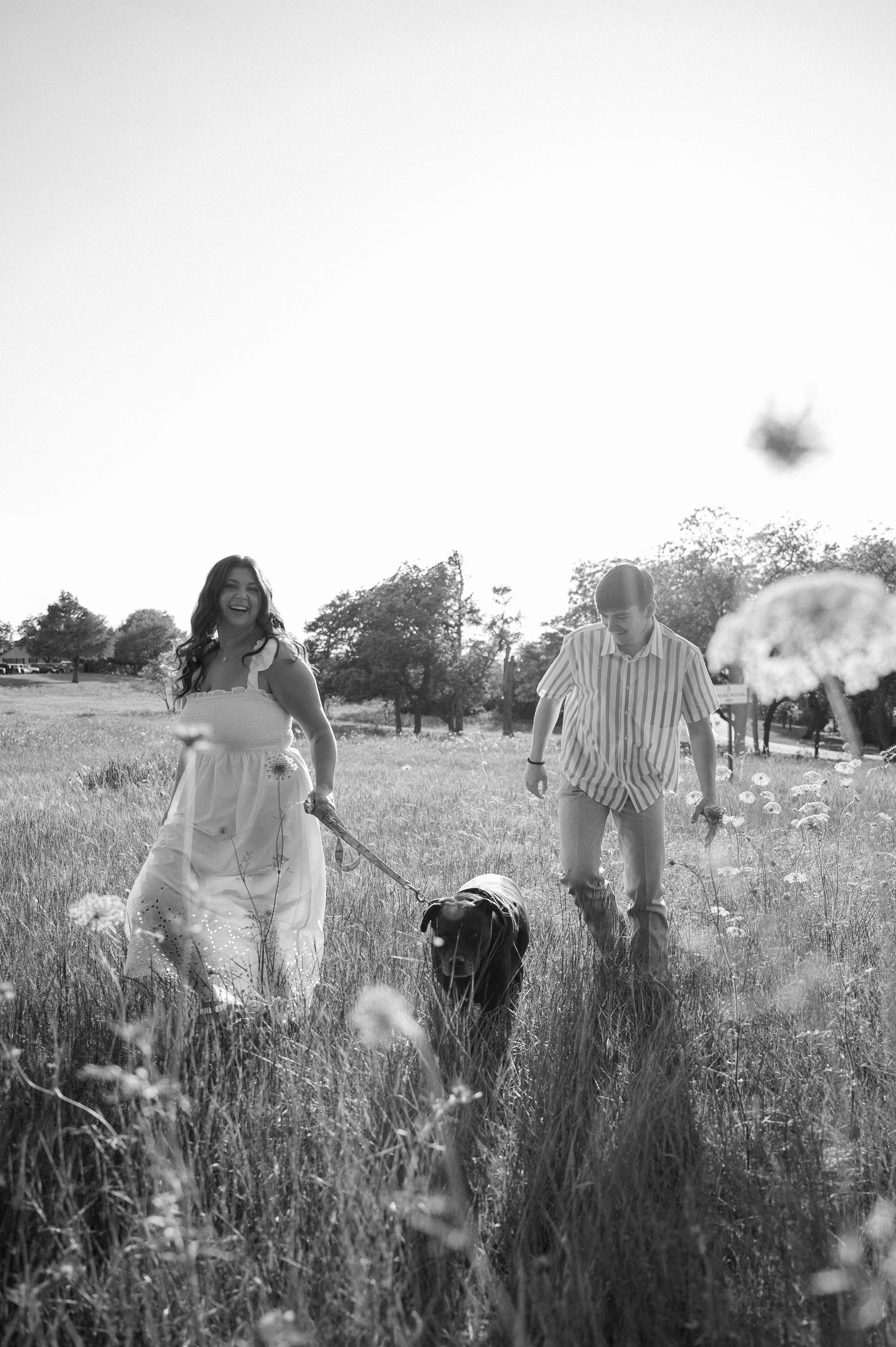 Black and white candid of a couple skipping through a wildflower field with their dog during a Spring engagement photo session