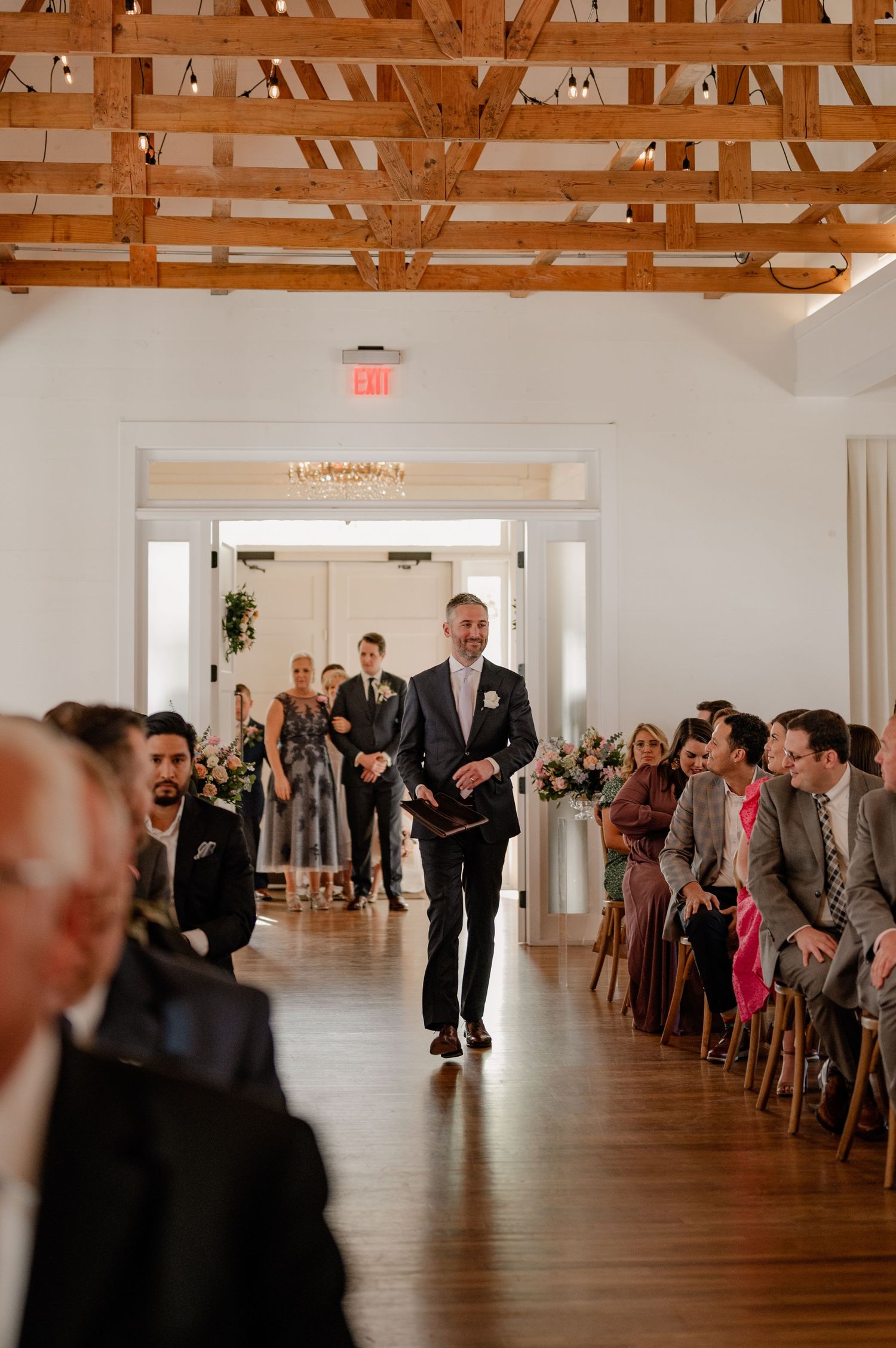 Wedding party and guests seated in rows at historic Dallas, TX venue while groom walks down the aisle for wedding ceremony