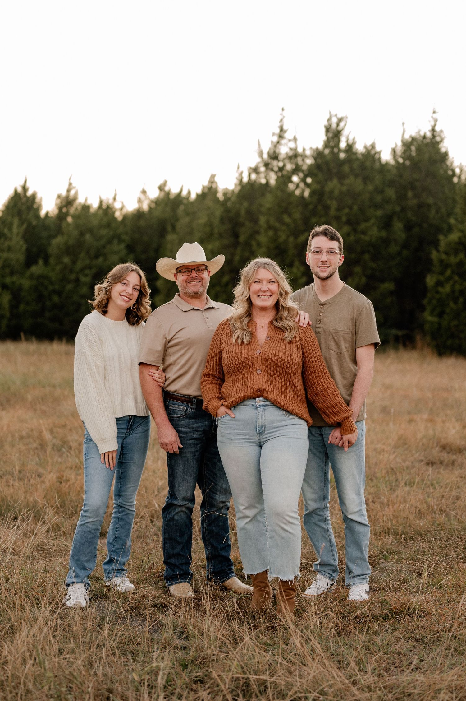Family of four posing for fall family photos in a large tree lined field in warm colors during blue hour