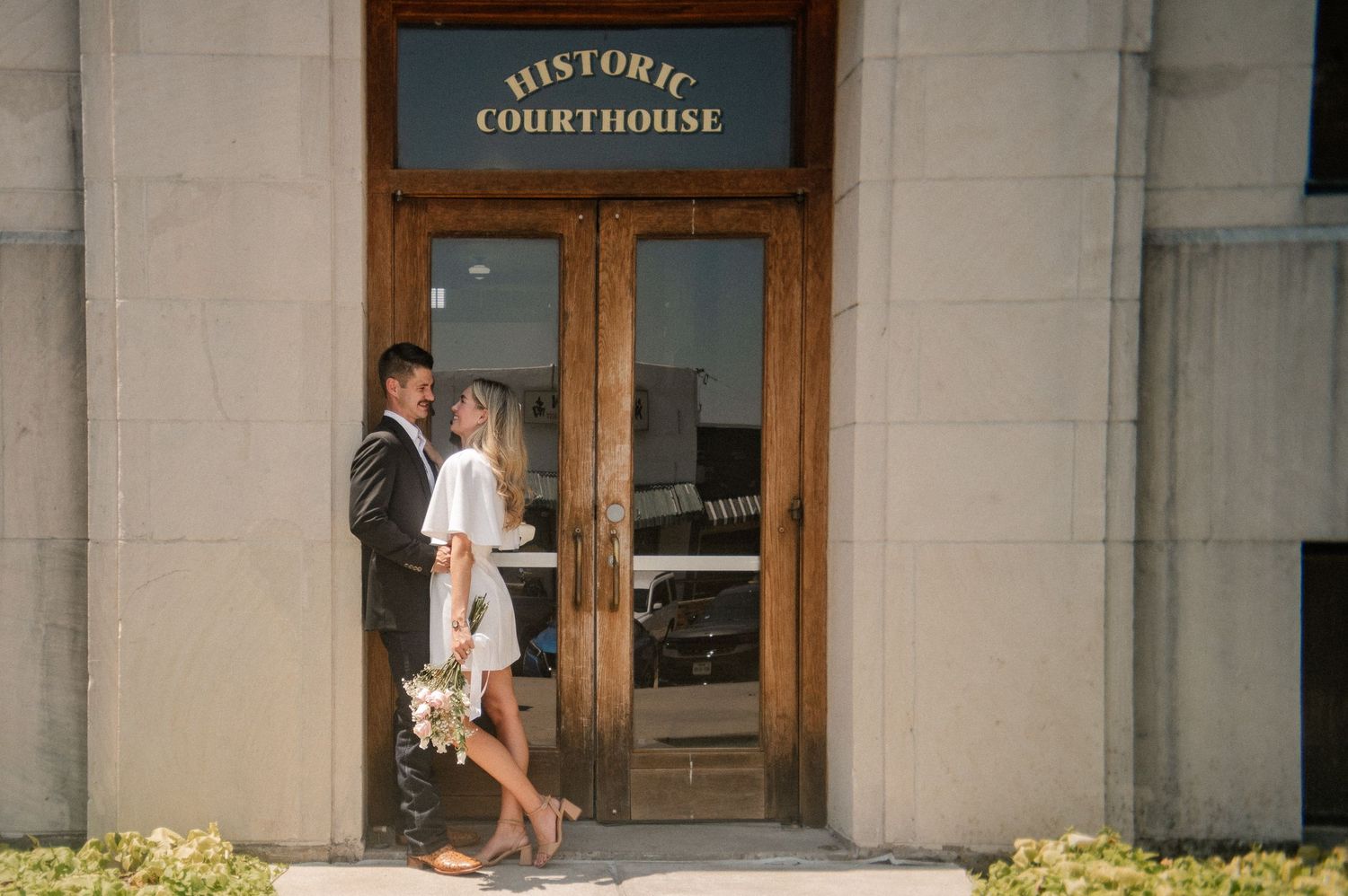 Film photo of couple posing outside in front of the downtown Rockwall courthouse during a summer elopement wedding photo session