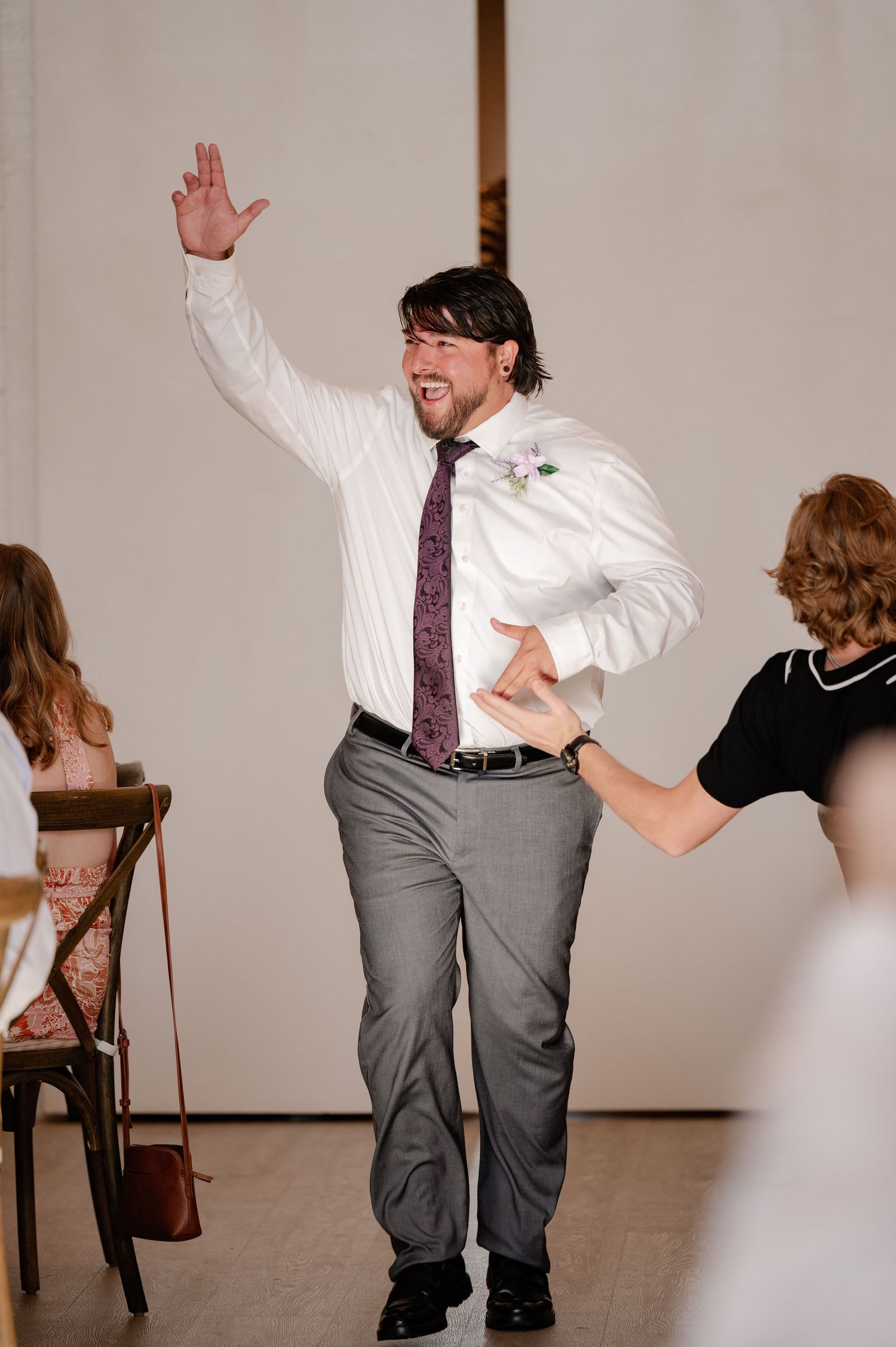 Groomsman energetically entering a wedding reception in a white shirt and purple tie