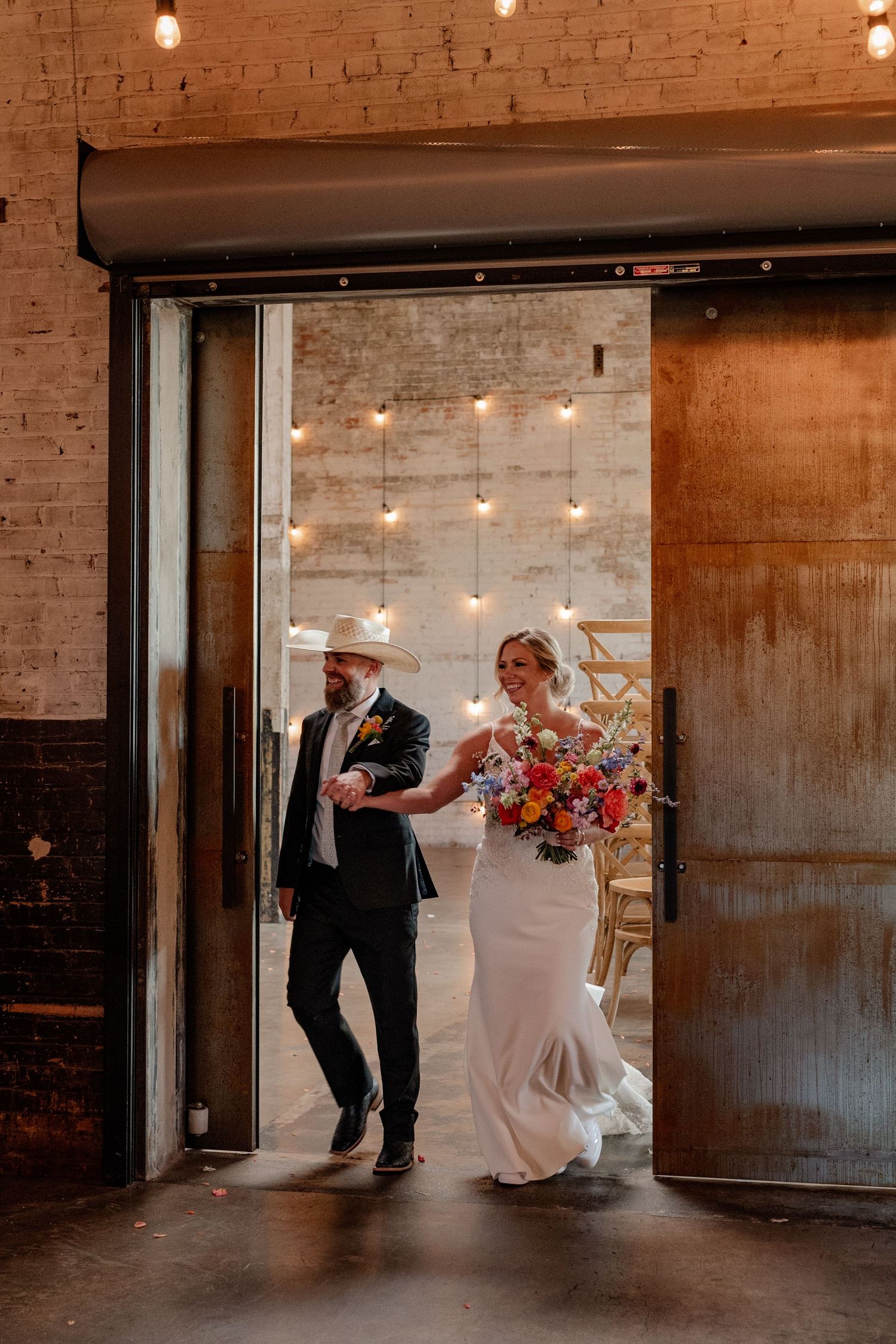 Bride and groom joyfully and candidly enter an industrial Downtown Dallas reception hall during their summer wedding