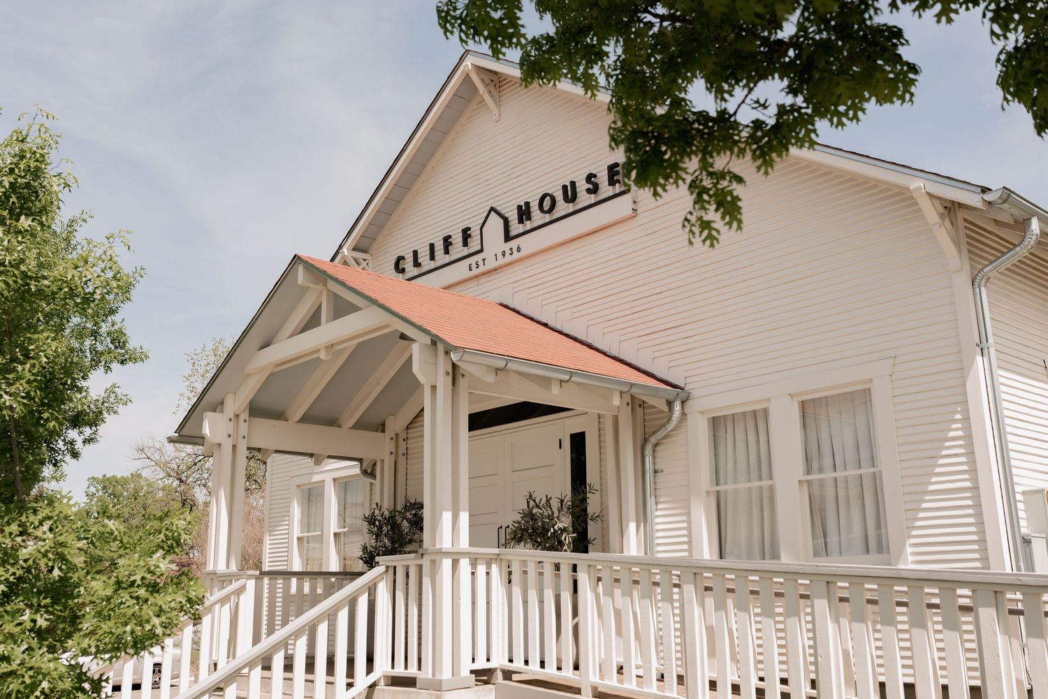 White vintage wedding venue with a wraparound porch and pillars under a blue sky