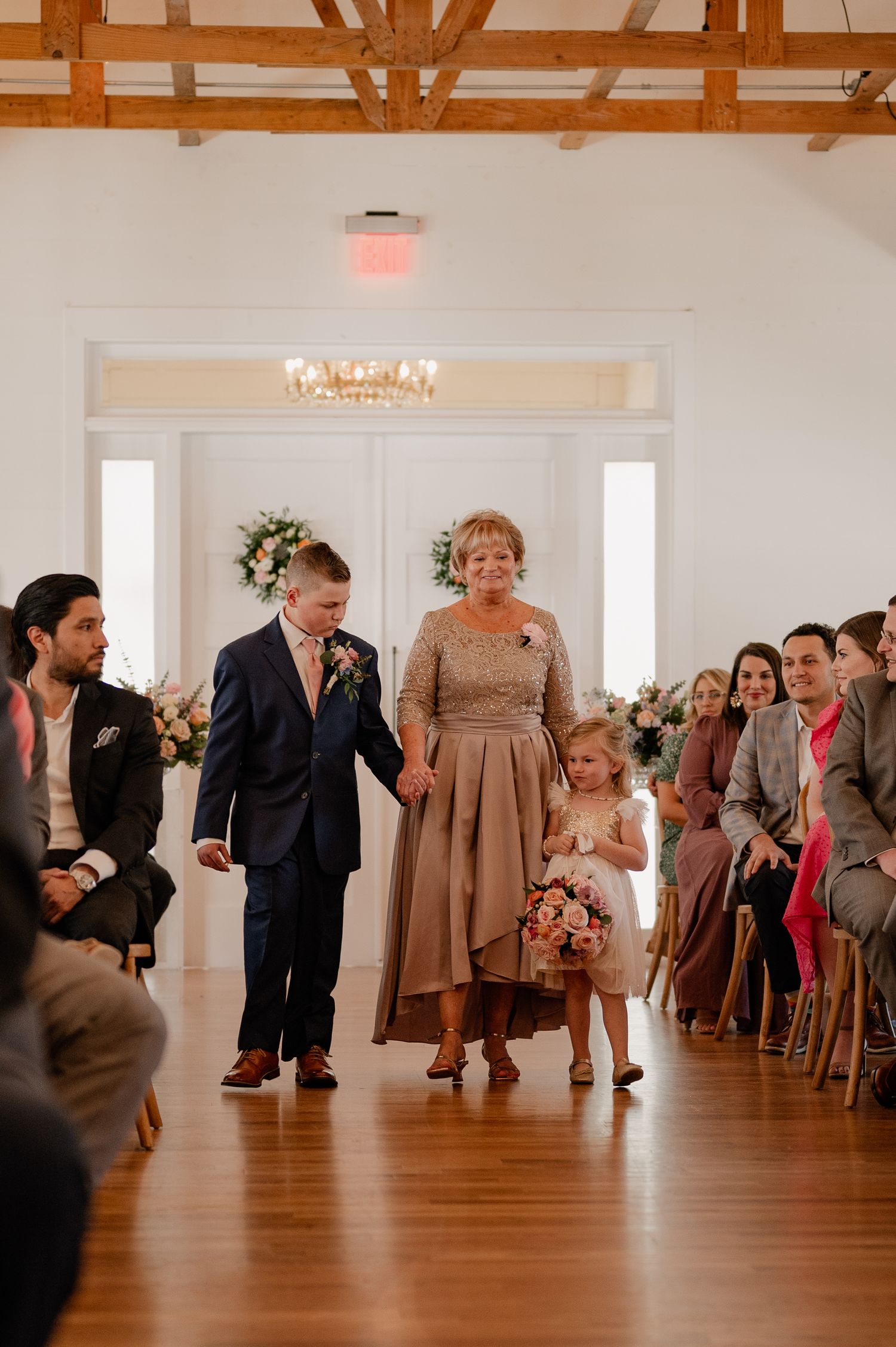 Wedding processional in a bright reception hall with wooden beam ceiling.