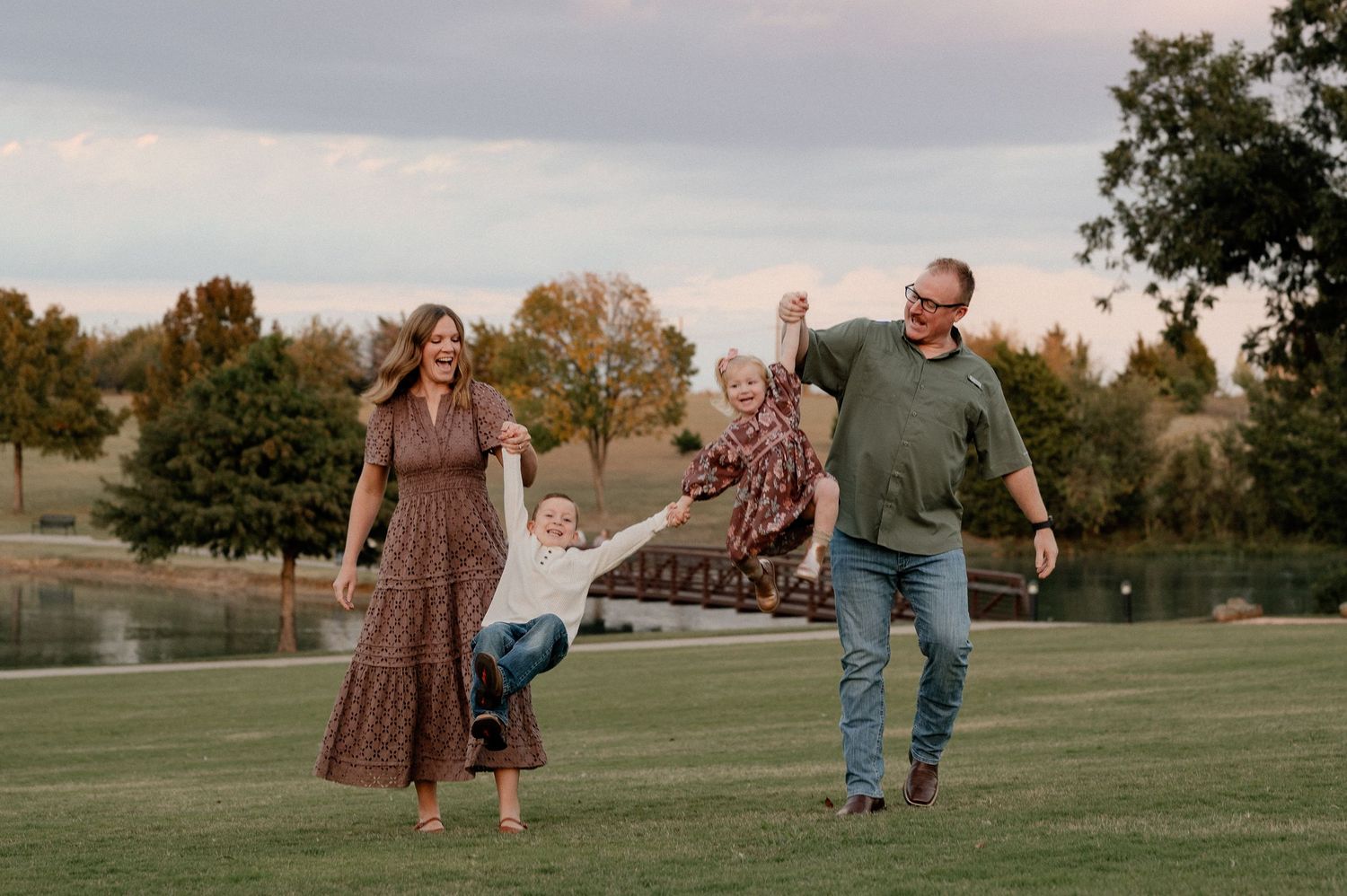 Family joyfully walking and playfully swinging kids at a park in Rockwall TX for an outdoor family photo session
