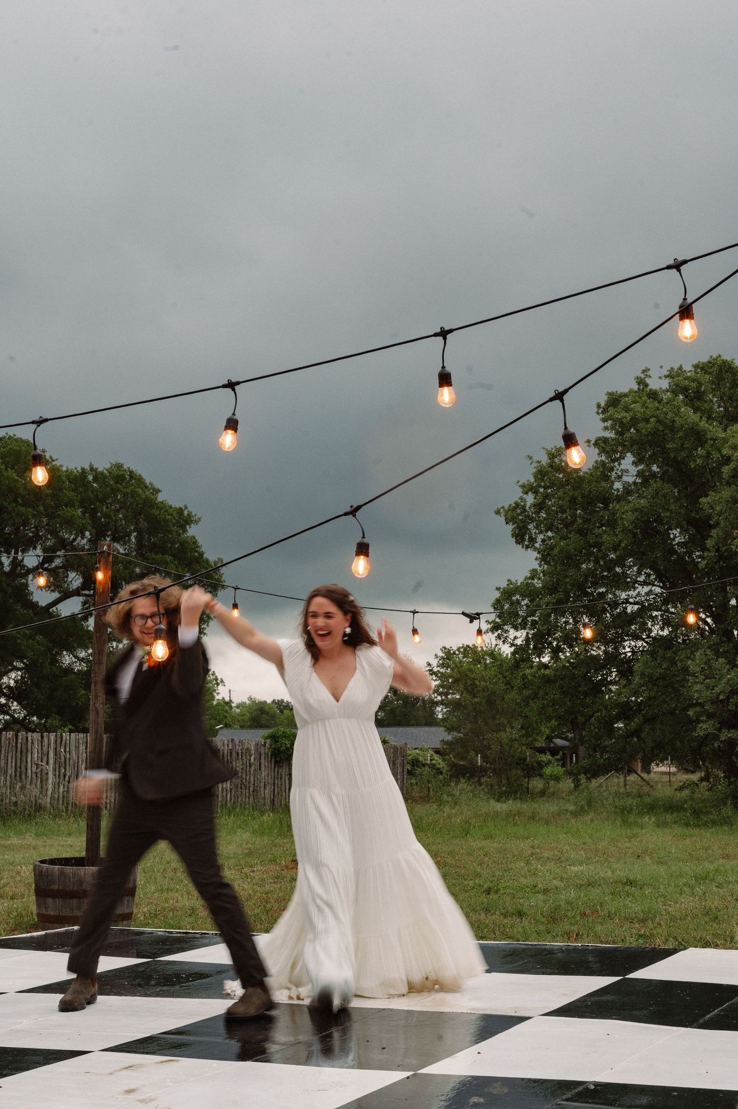 Joyful blurry candid of a wedding couple on an outdoor reception dance floor for their first dance in a rainstorm near Ft. Worth, TX