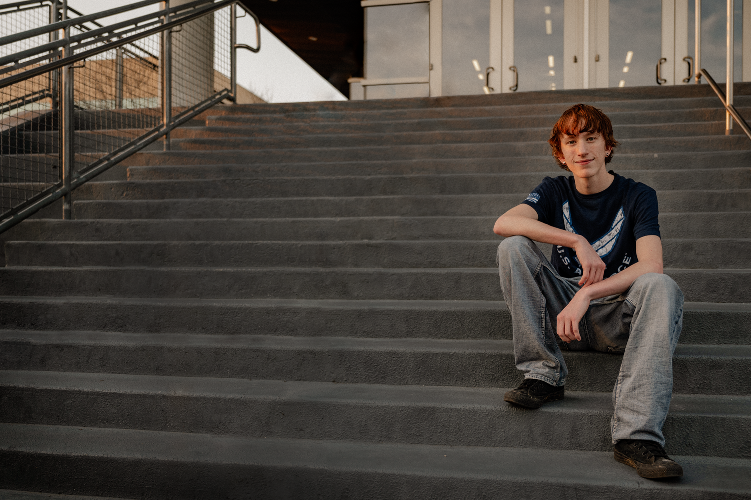 Senior sitting on a concrete staircase wearing college tshirt for an industrial senior photo session in Richardson, Texas at UT Dallas