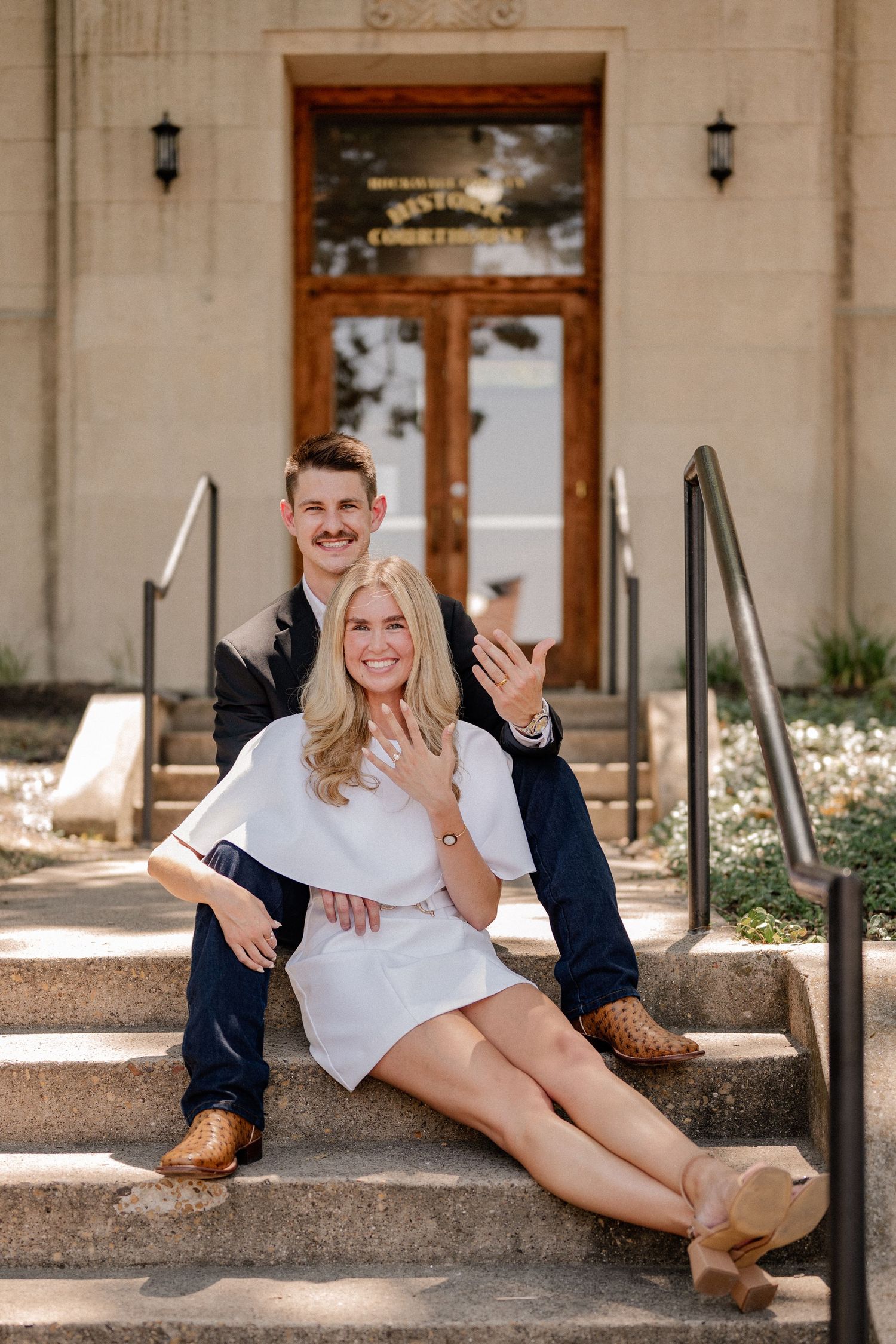 Couple sitting on staircase showing off their rings outside of the downtown Rockwall courthouse during elopement wedding photo session