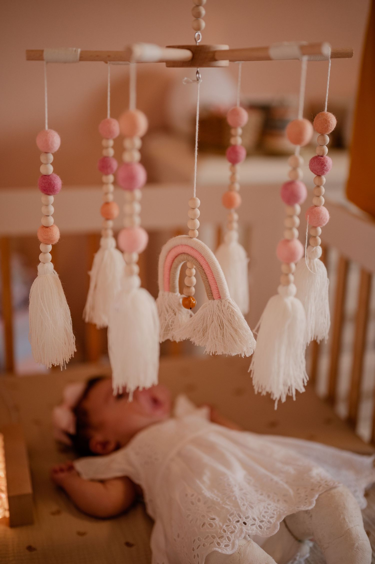 Delicate pink and white tassel mobile hangs above crib in nursery setting.