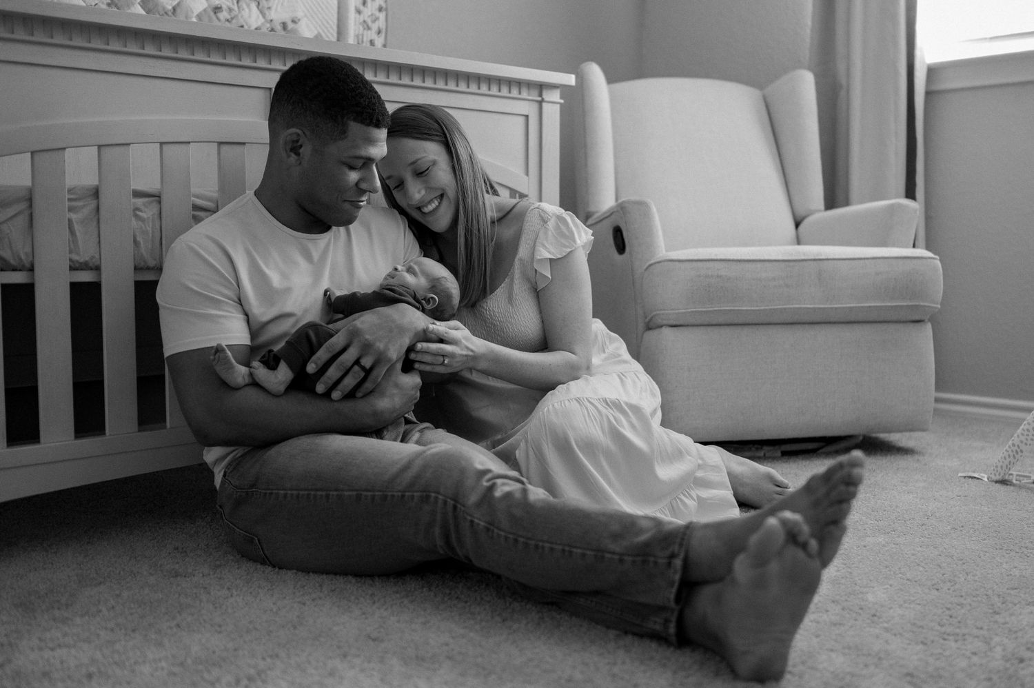 Black and white photo of new parents holding their newborn baby sitting in on the floor of their nursery for a newborn at-home photo session