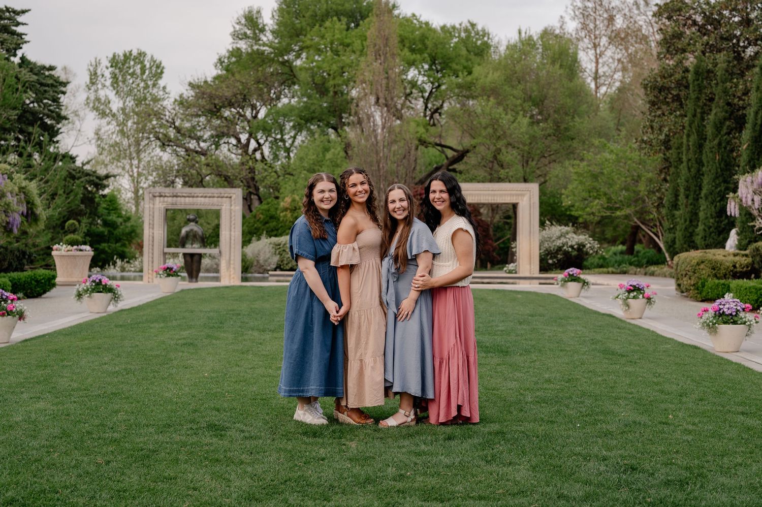 Four sisters posing in a line in a green field with modern architecture in the background for their summer family photo session