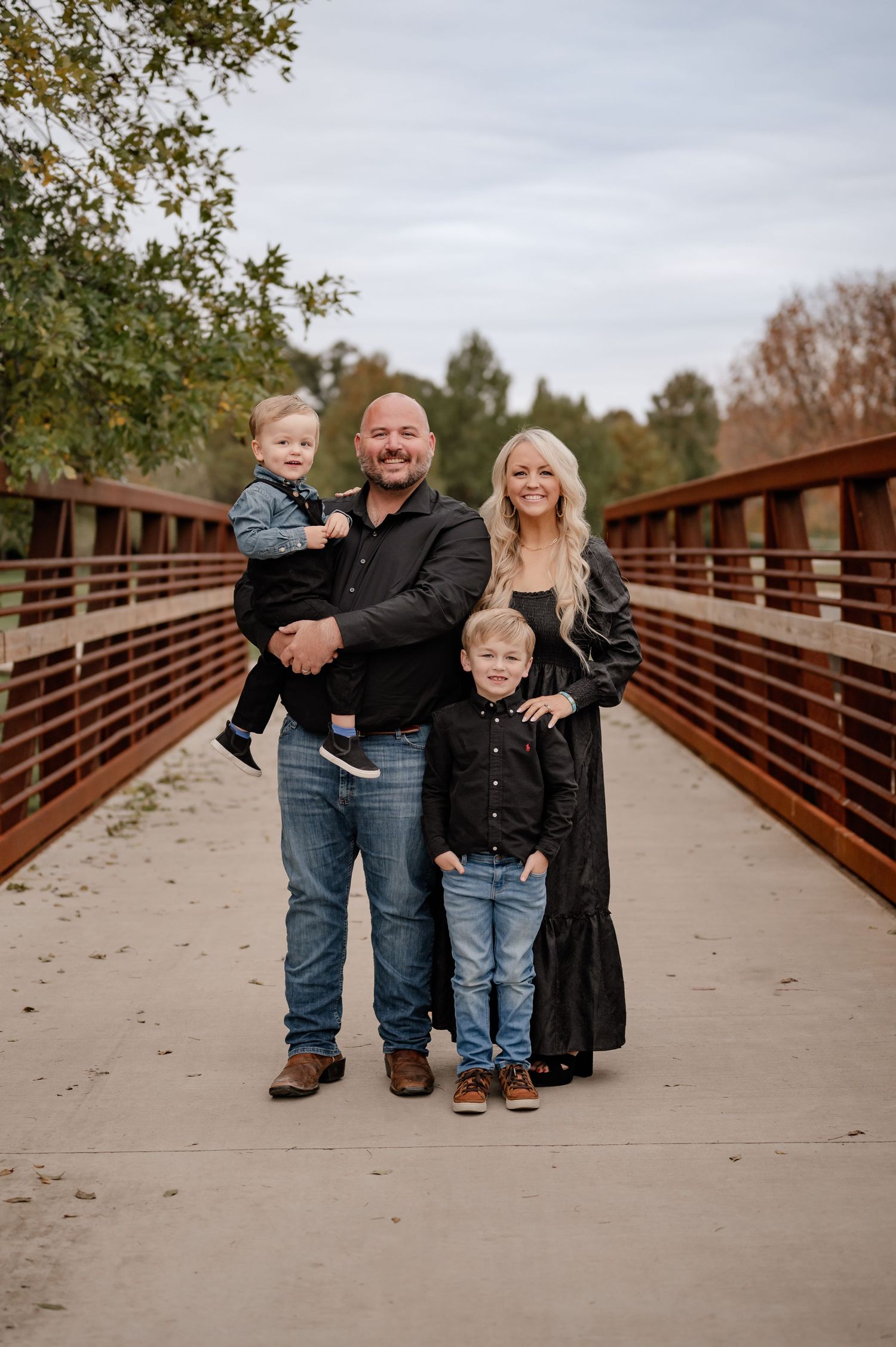 Family standing in the middle of a large industrial bridge in black outfits for a winter family photo session in Dallas, Texas