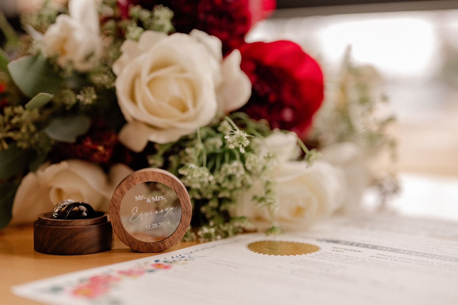 Wedding rings displayed alongside elegant white and red roses with decorative greenery in soft lighting.