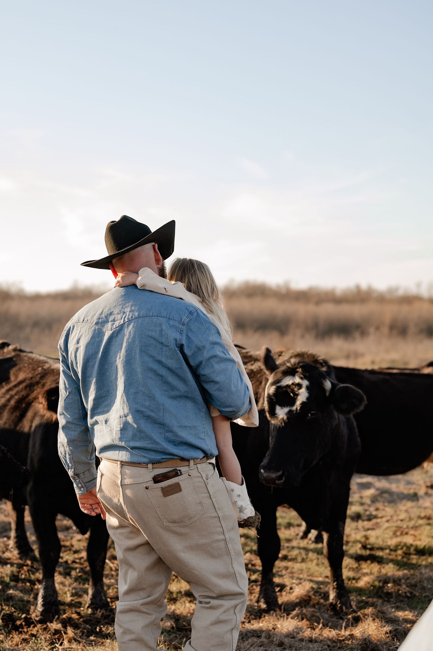 Dad in cowboy hat holding his daughter overseeing his cattle on his cow farm in Rockwall, Texas during at at-home fall family session