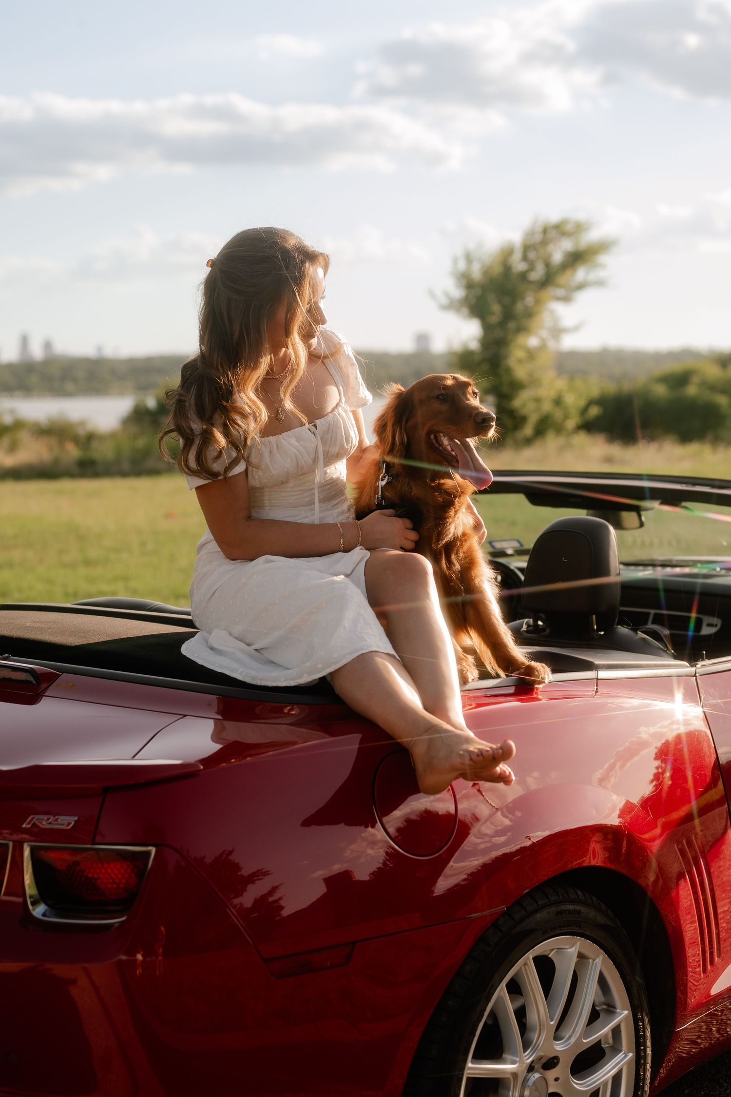 Candid of woman and her golden retriever   hanging out of the back of her red Corvette  with White Rock Lake in the background