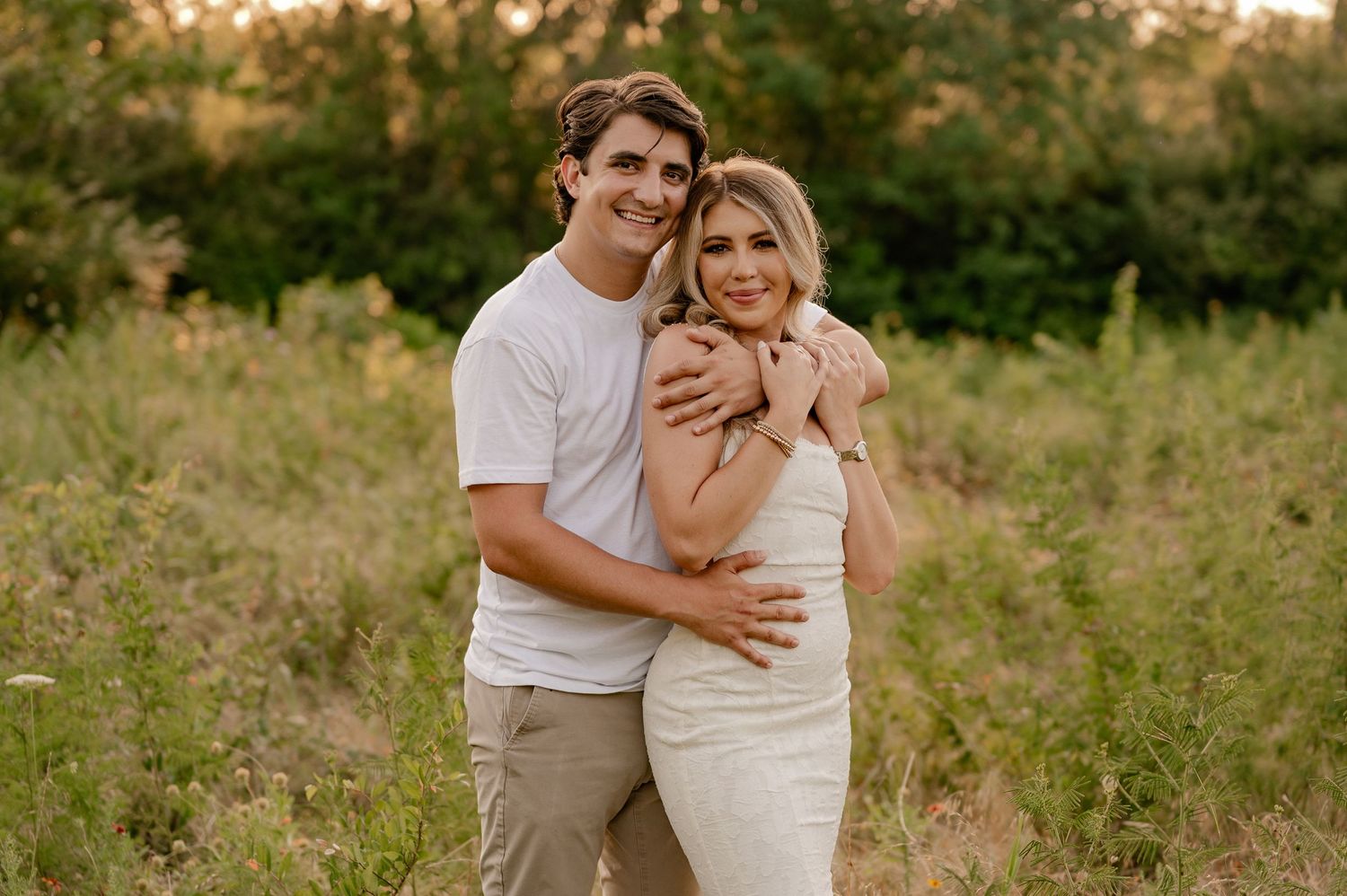 Couple embracing in a Dallas, Texas meadow at sunset, surrounded by lush greenery for an engagement photo session