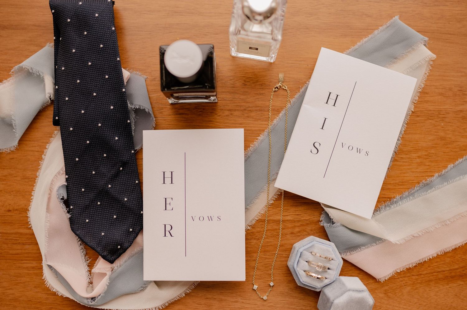 Wedding details including tie, rings, perfumes, and invitation suite arranged on wooden surface