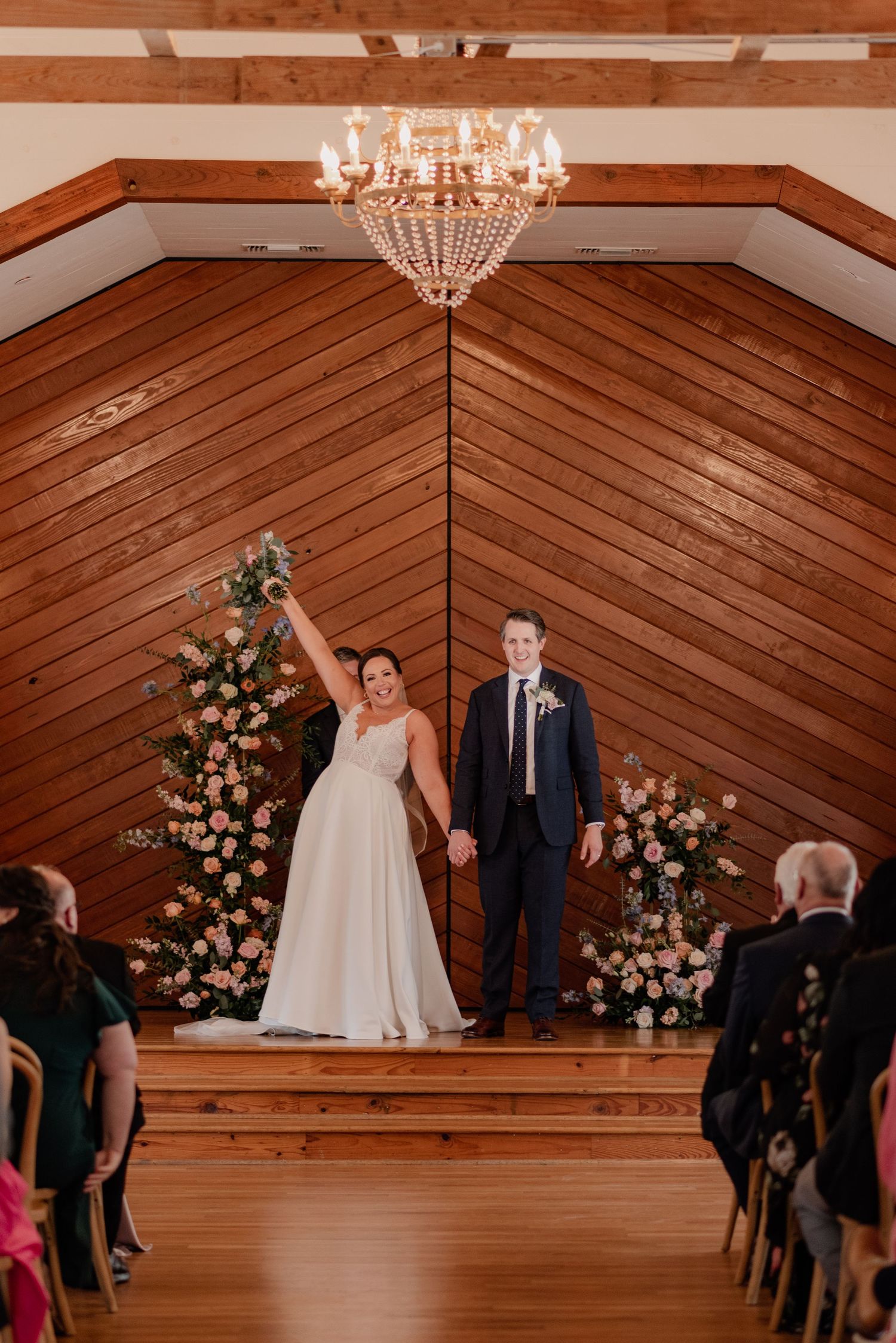 A grand chandelier hangs in a wooden chapel as newlyweds celebrate at their wedding ceremony.