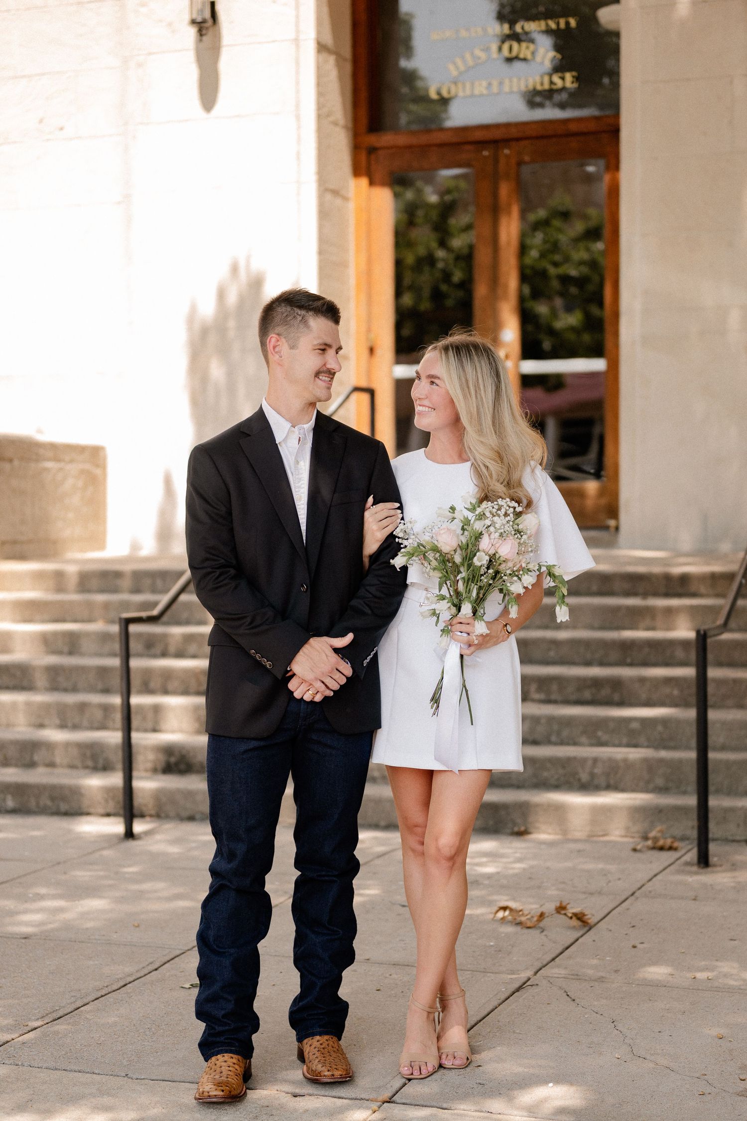 Married couple posing in front of a staircase outside of the downtown Rockwall courthouse during elopement wedding photo session