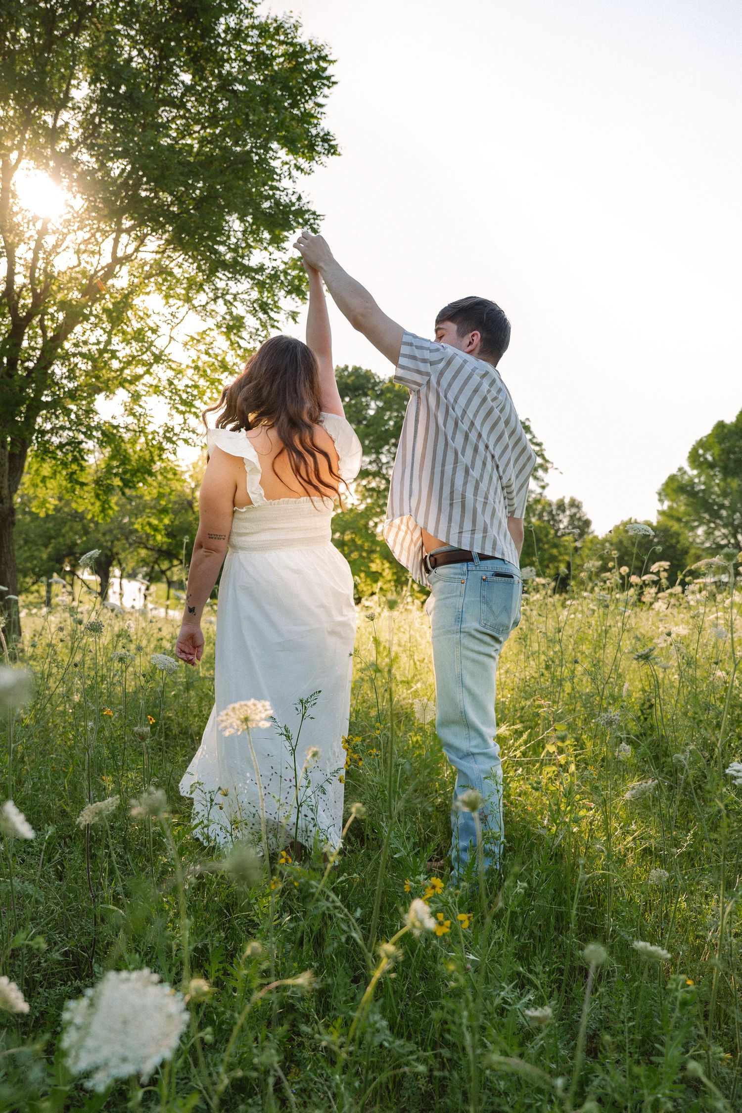 Couple dancing and spinning in tall wildflowers with the sun peeking through the trees for an engagement session in Dallas, Texas