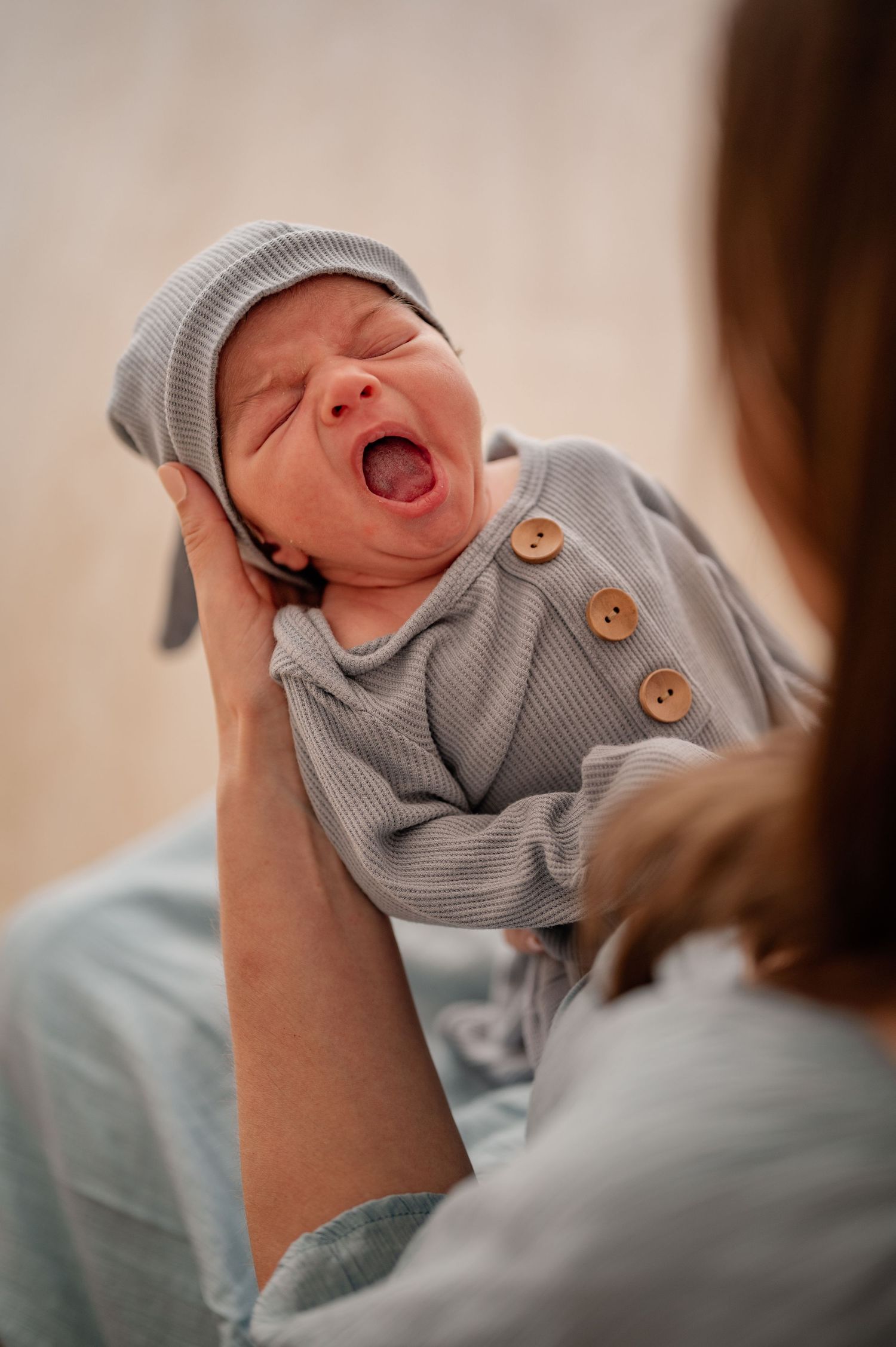 Newborn baby wearing gray knit outfit yawning during photoshoot.