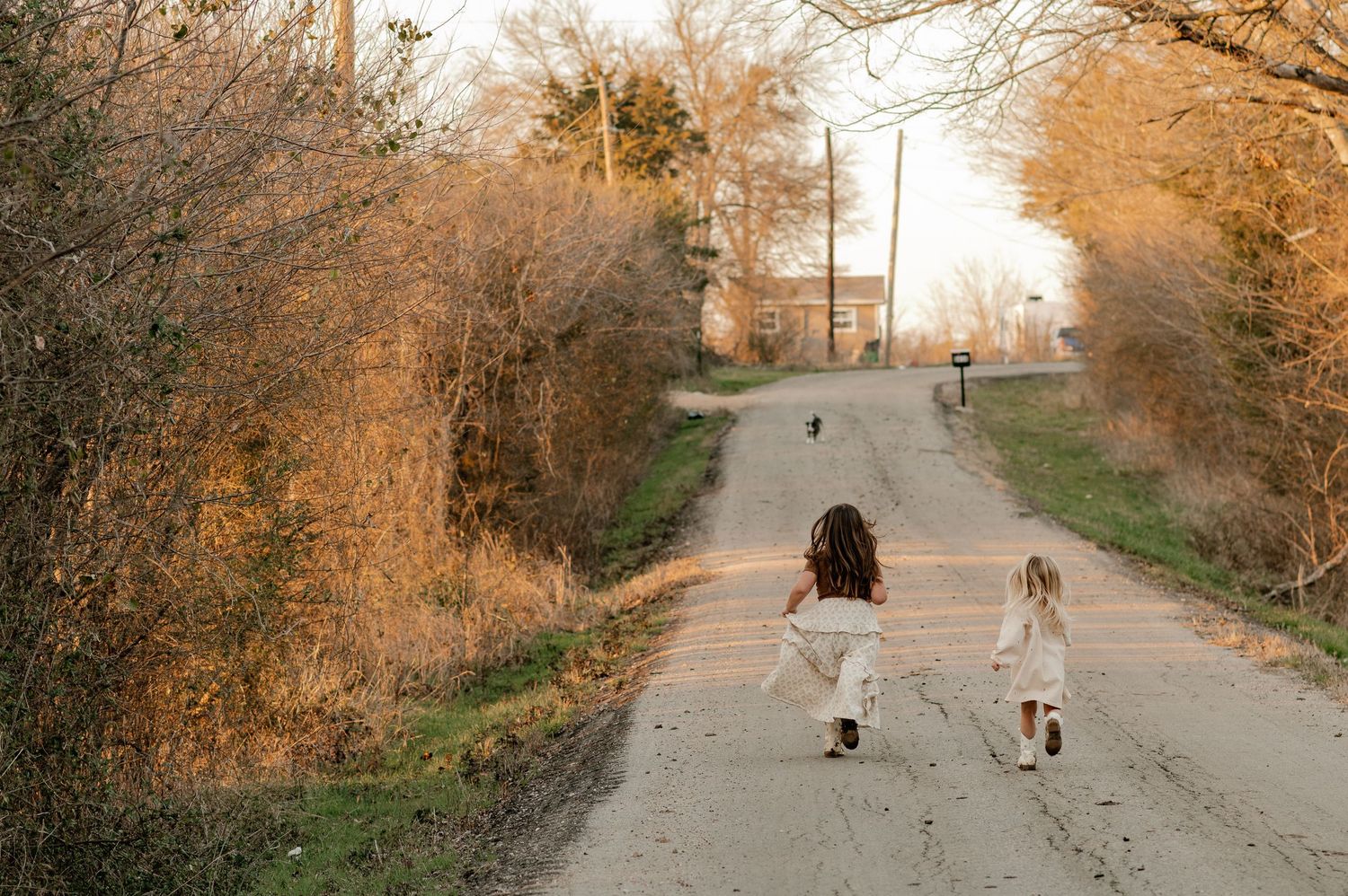Candid lifestyle photo of 2 girls running down a long road out in the country for an at-home family session in Greenville, Texas