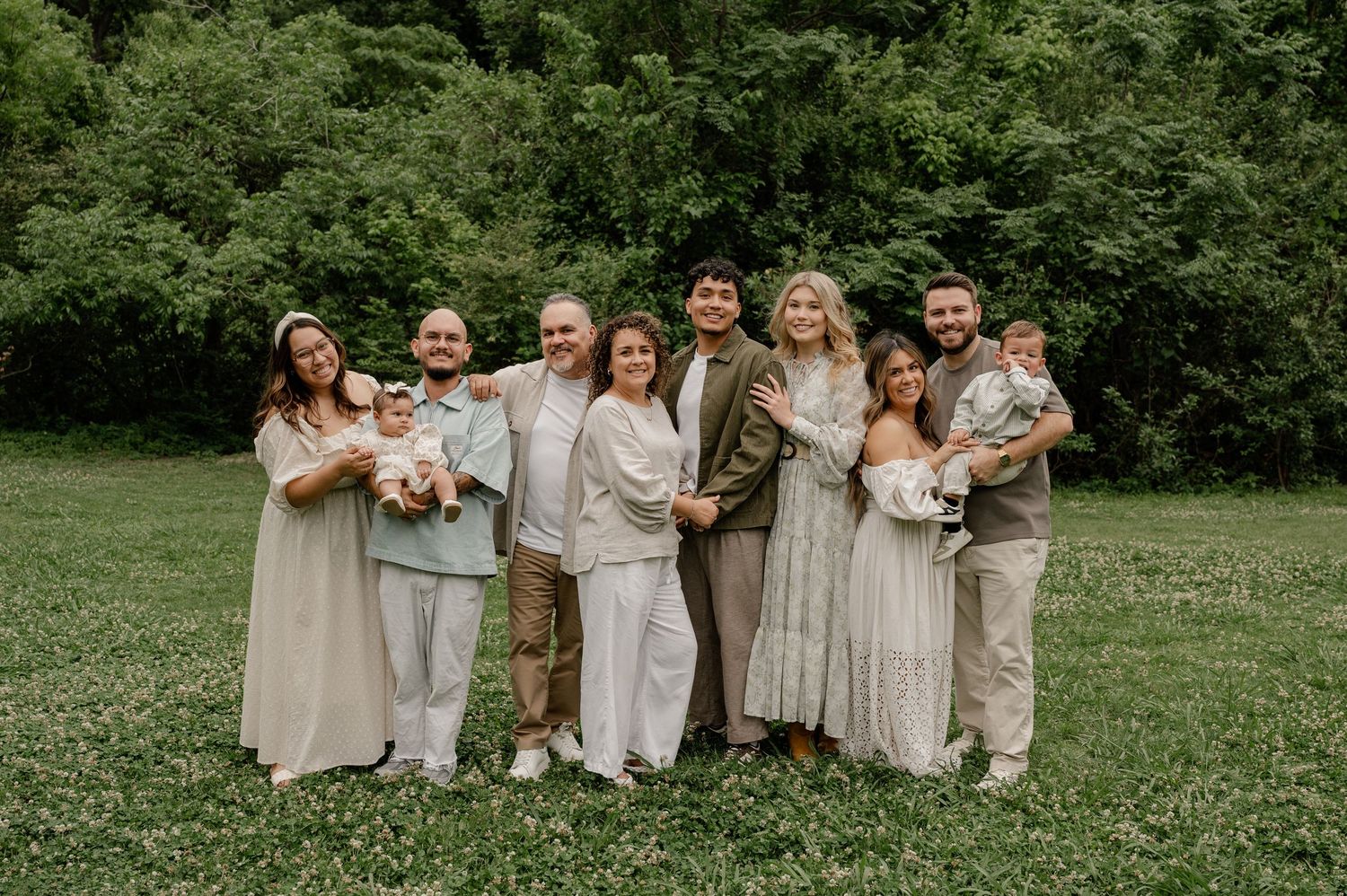 Large extended family posed in a line in a  green park space for a family photo session in Richardson, Texas