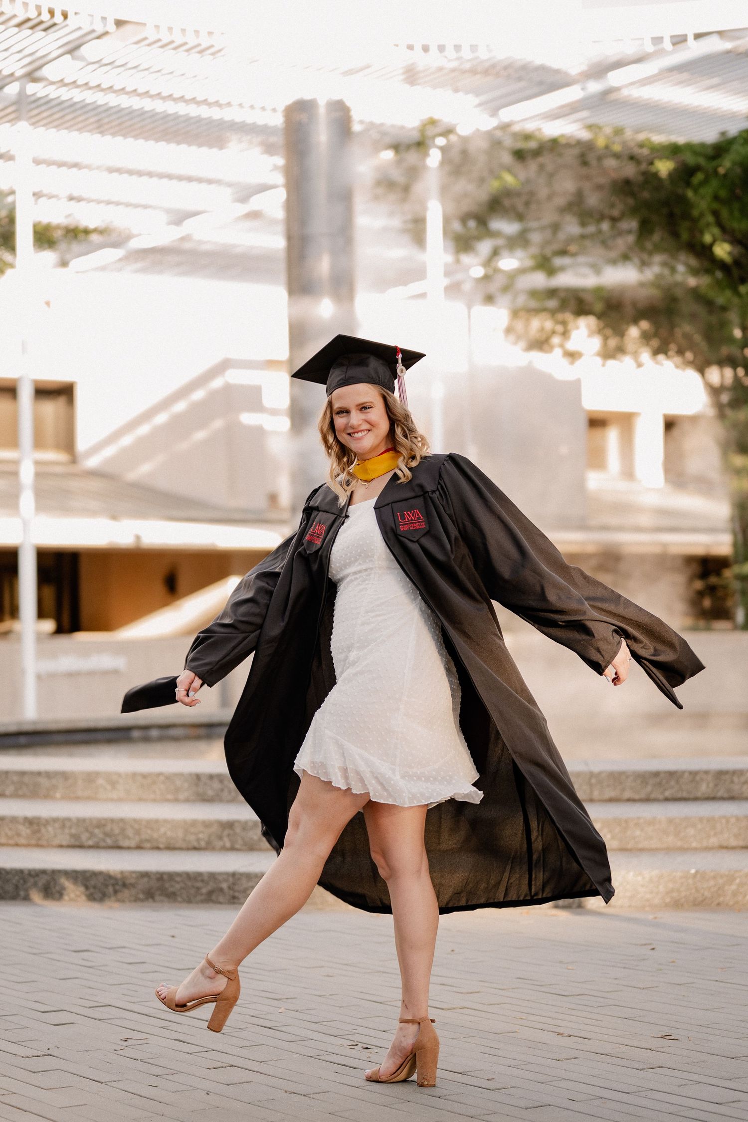 College senior girl playfully posing in cap and gown at University of Texas at Dallas for a fall senior photo session