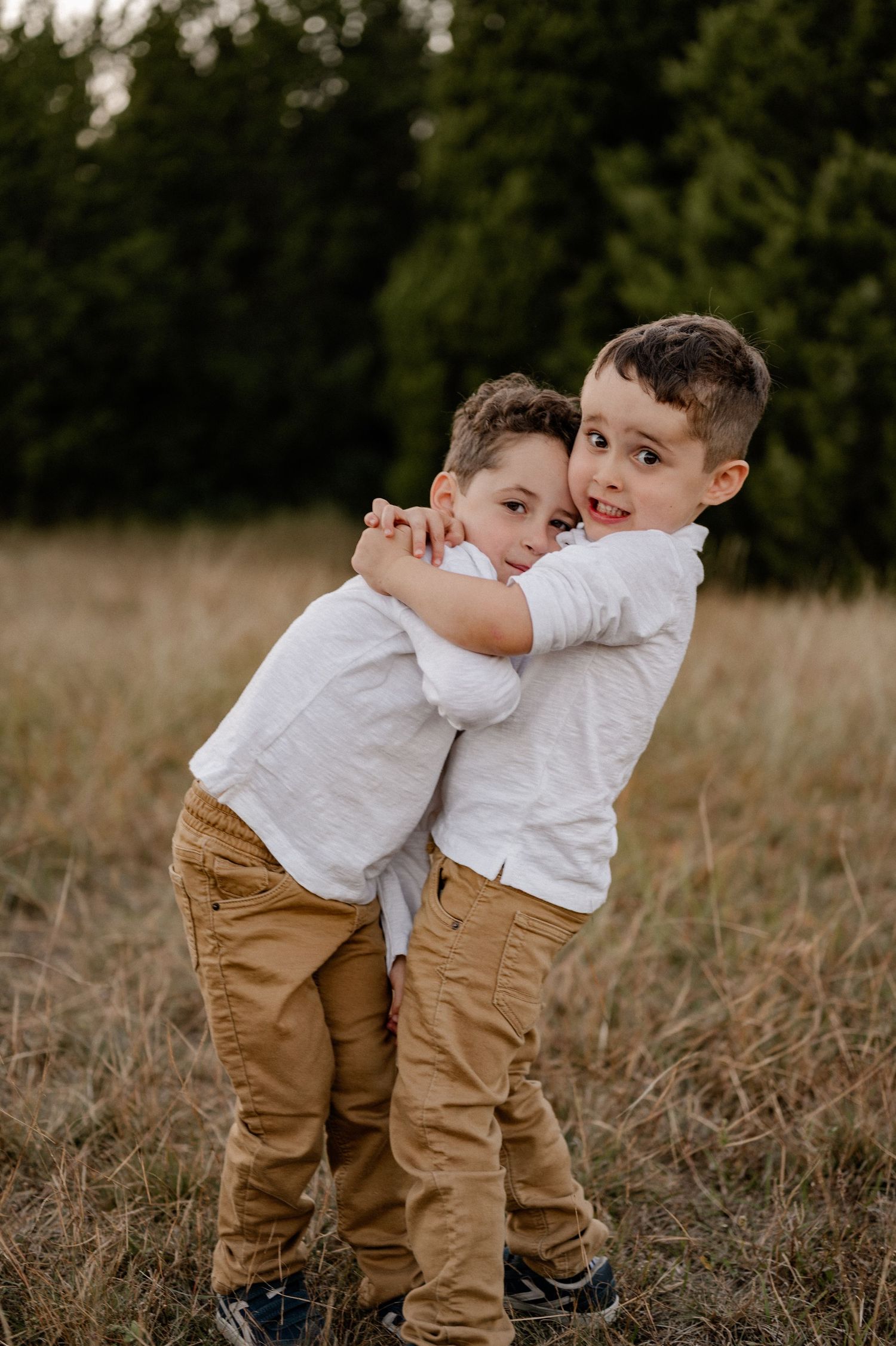 Brothers aggressively hugging in a large field lined with trees at an outdoor family session for fall photos in Sunnyvale, Texas