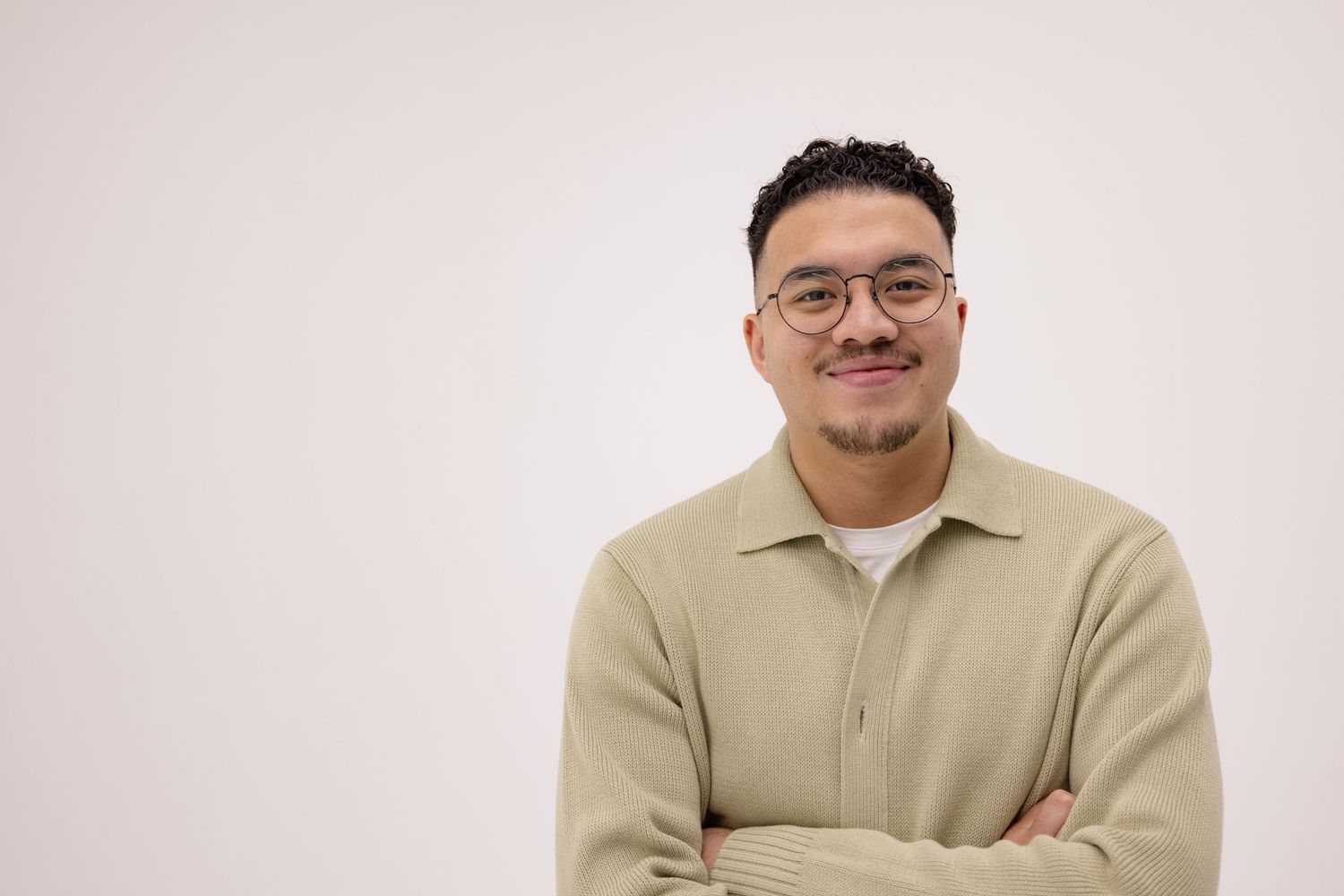 A tight smiling headshot portrait of a male musician in front of a white studio wall