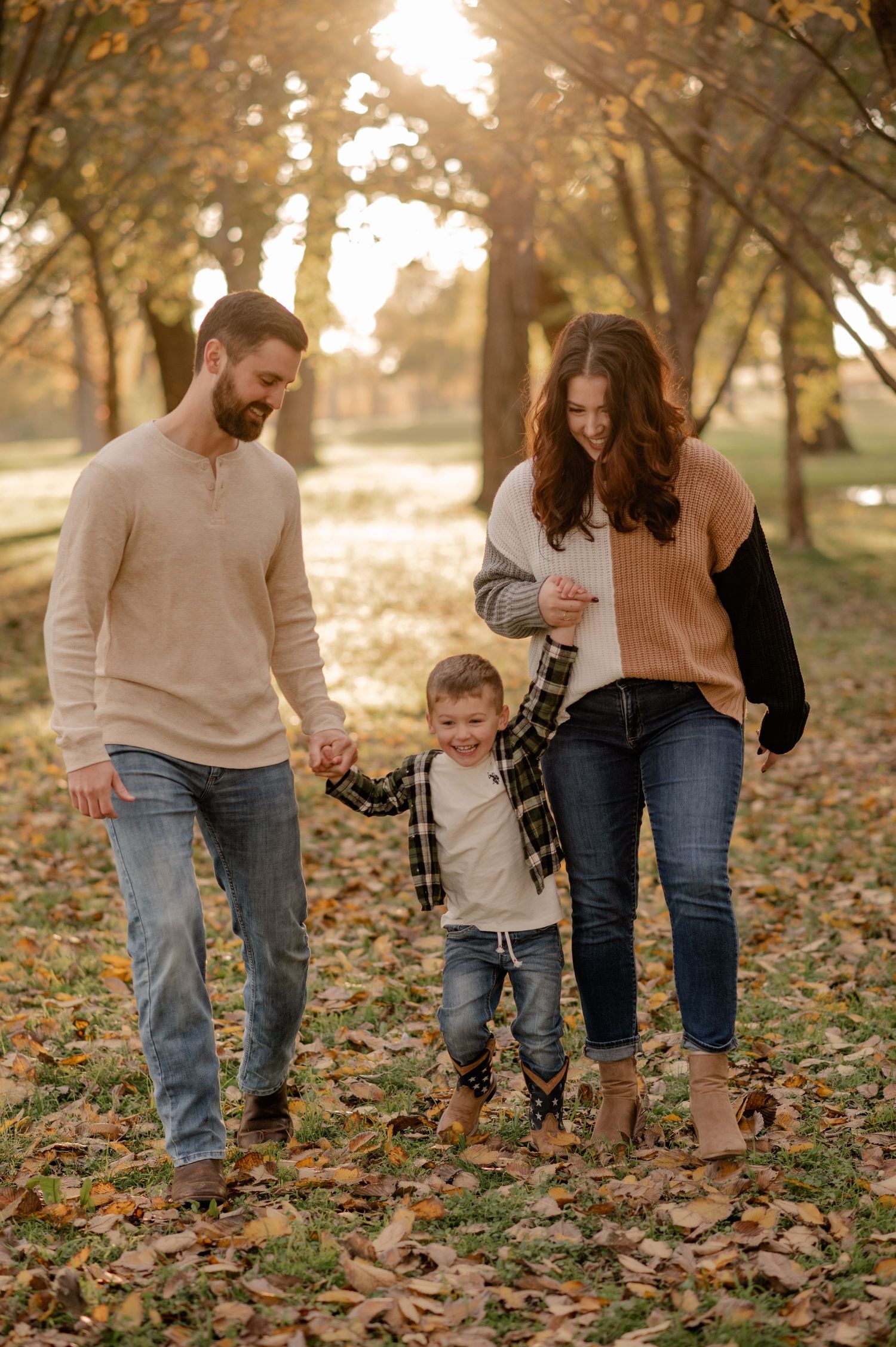 Family of 3 candidly holding hands walking through fallen leaves at golden hour for a Fall family photo session in Dallas, Texas