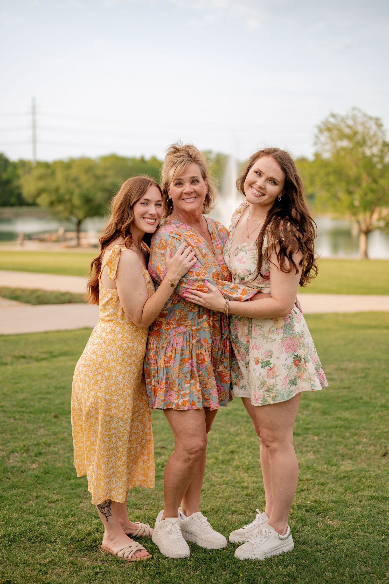 Mother and two daughter posing for Spring family photos in vivid colors at large park with water feature in Rockwall, Texas