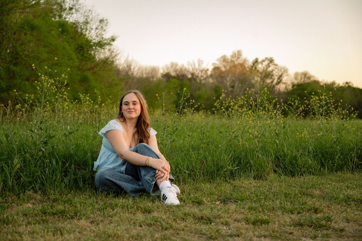 Senior girl sitting in a tall wildflower field in Spring wearing casual clothes in a Spring Senior photo session in Richardson, Texas
